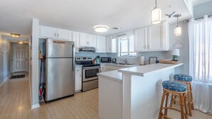 A modern kitchen with white cabinets, stainless steel appliances, and a central island with bar stools. - Sunskipper by Carolina Retreats (Carolina Beach)