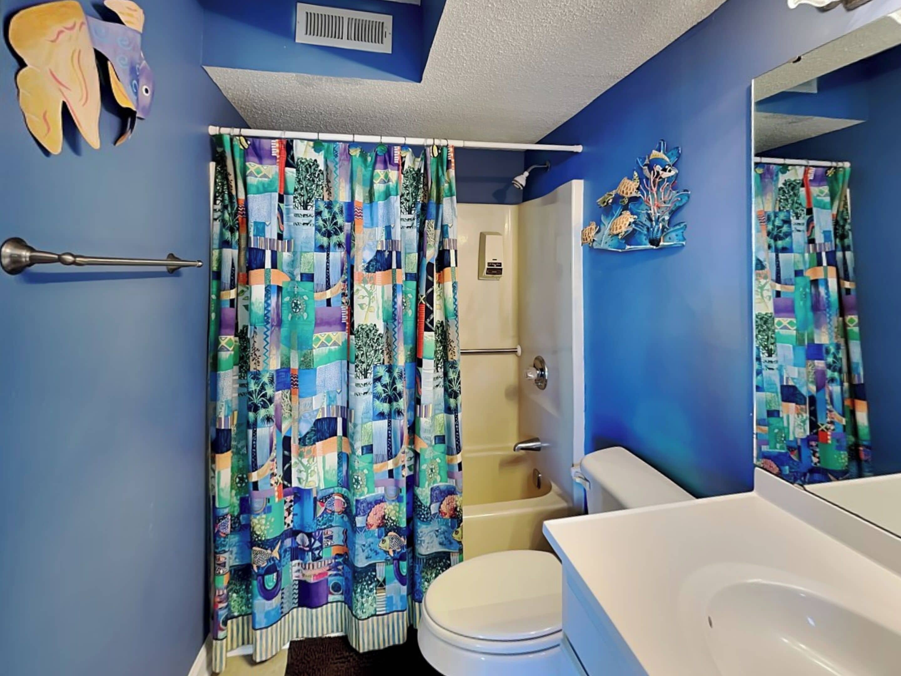 A bathroom with a blue wall, a white toilet, a white sink, and a shower with a colorful curtain.