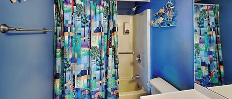 A bathroom with a blue wall, a white toilet, a white sink, and a shower with a colorful curtain.