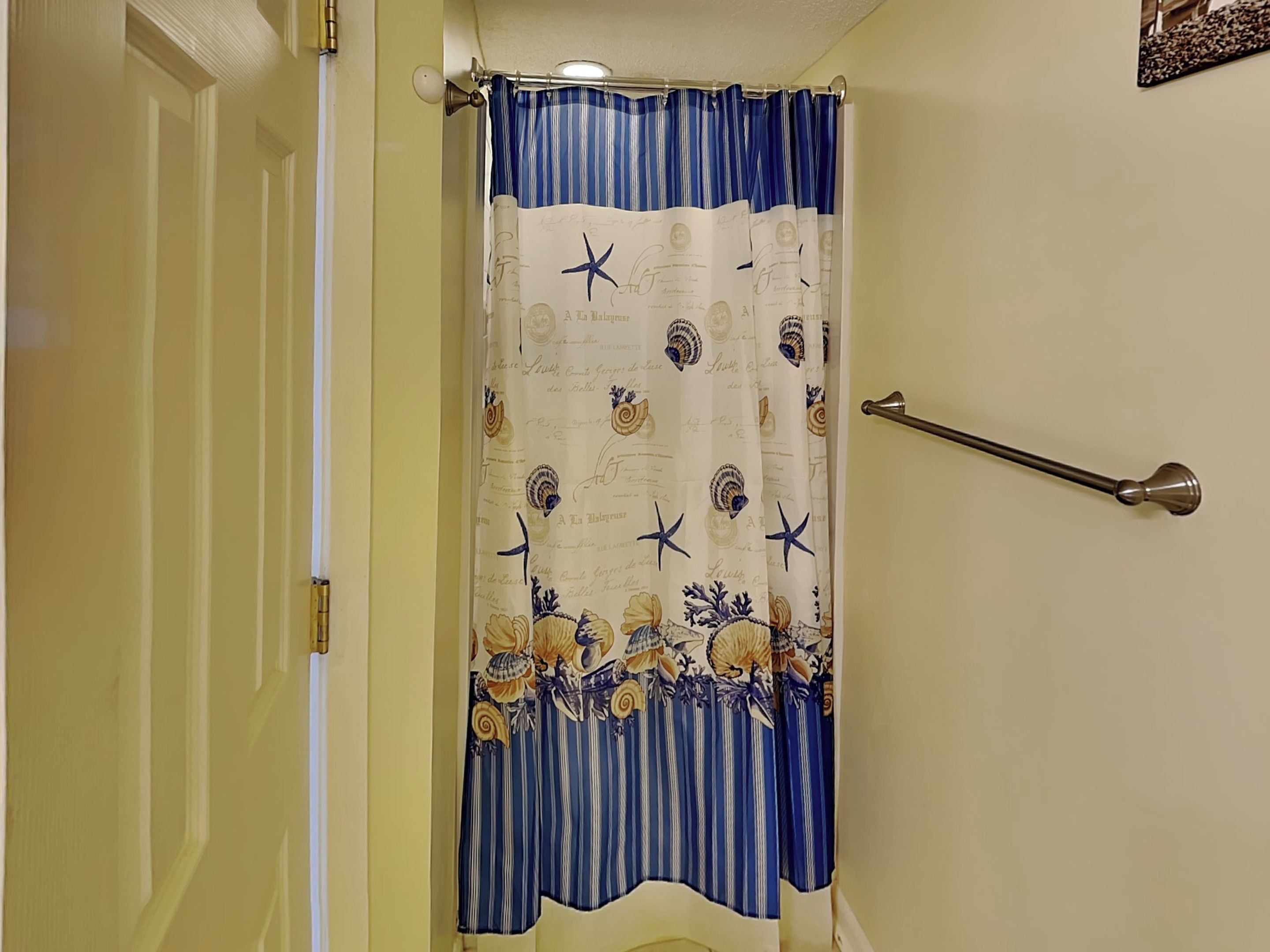 Un bagno con tenda da doccia a righe, decorata con conchiglie e stelle marine, un porta asciugamani e una porta.