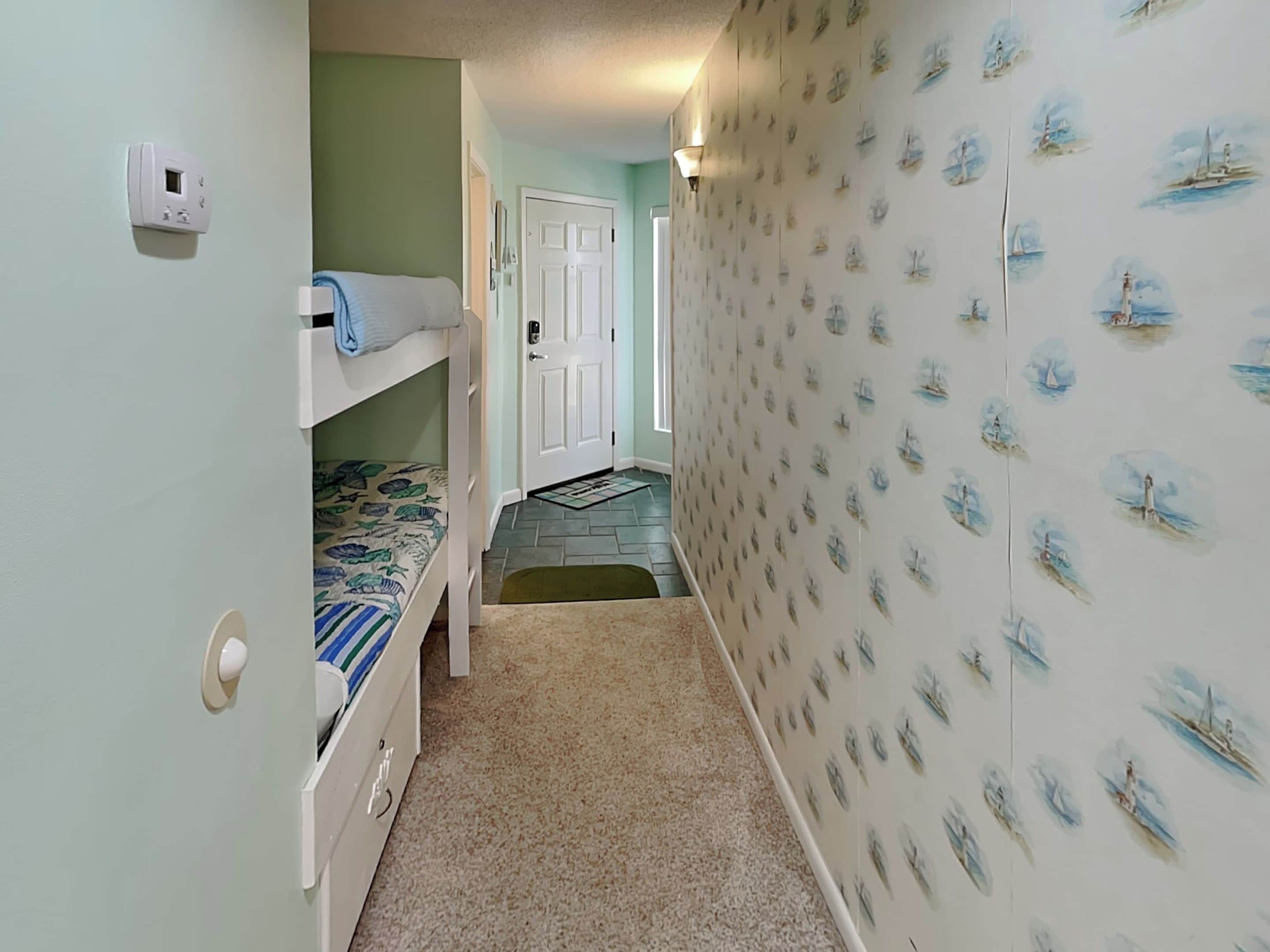 A narrow hallway with a bunk bed on the left, a door at the end, and a wall with maritime-themed wallpaper.