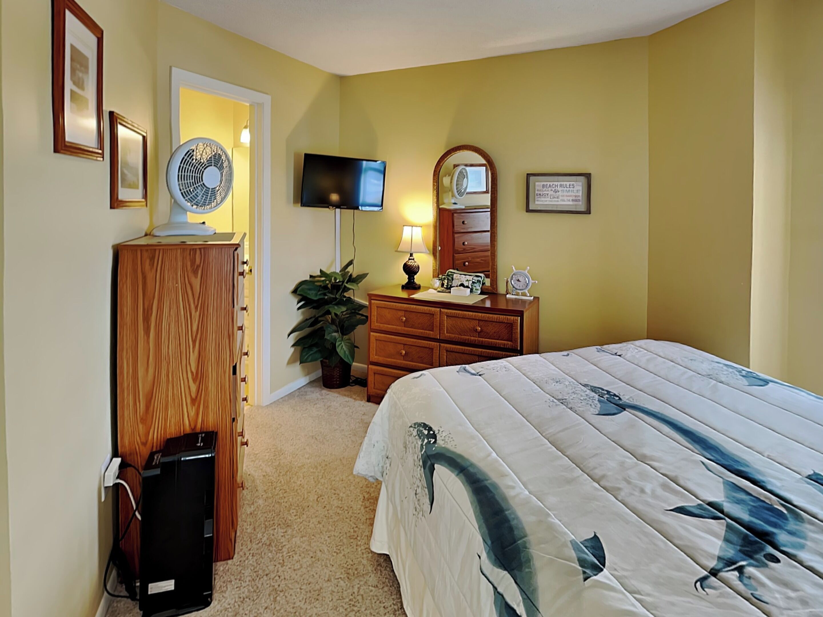 A bedroom with a bed, dresser, television, and a mirror.