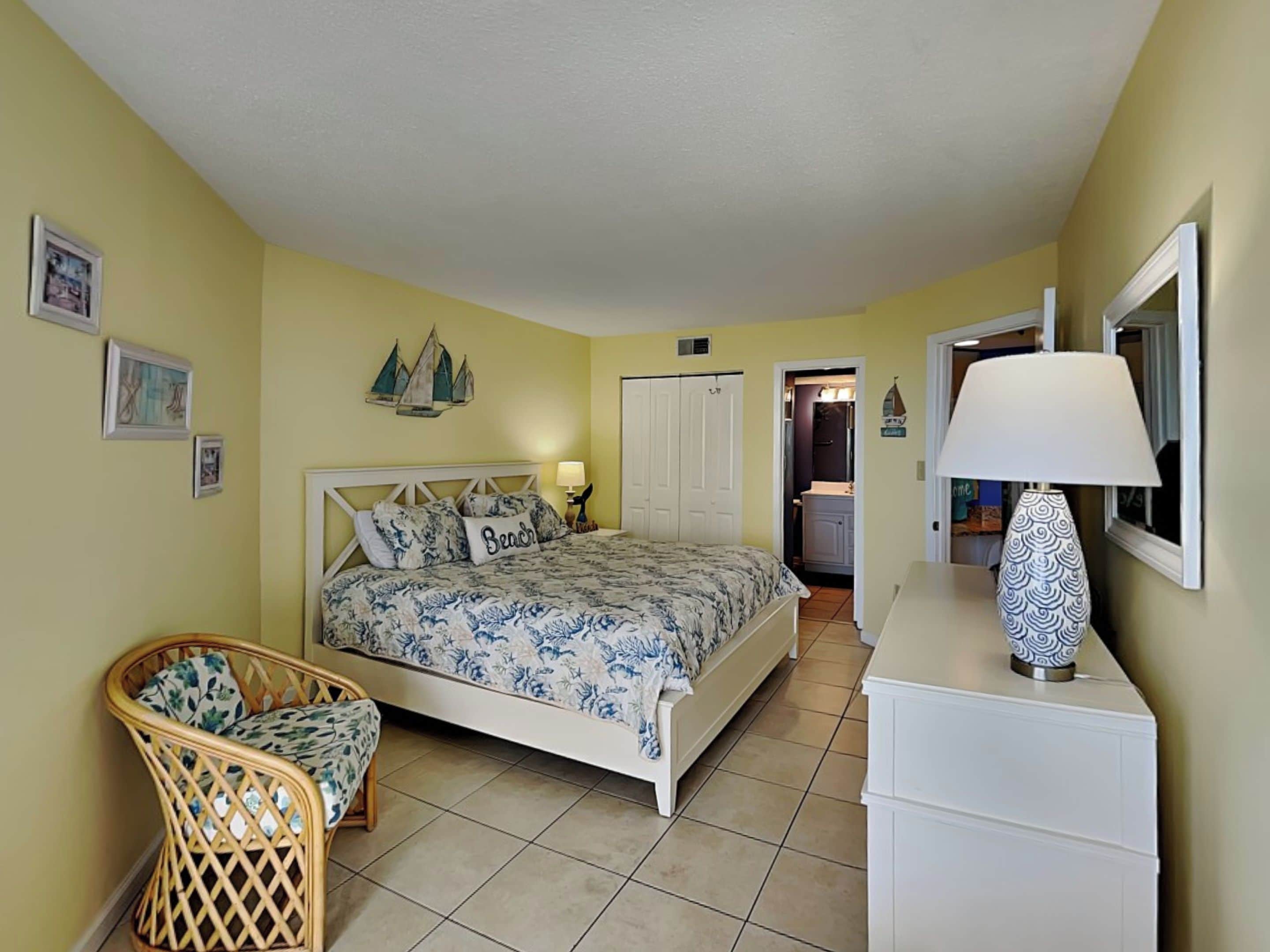 A bedroom with a bed, a chair, a dresser, and a lamp.