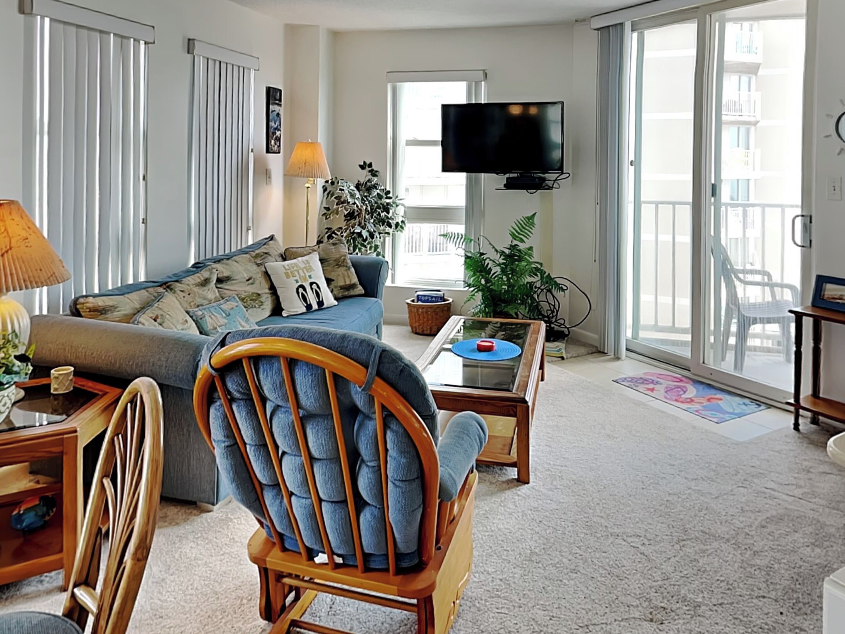 A living room with a sofa, a wooden chair, a coffee table, a TV, and a balcony with a view.
