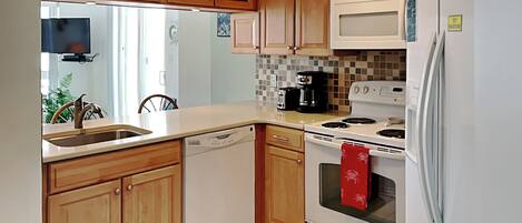A kitchen with wooden cabinets, a white refrigerator, a stove, and a dishwasher.