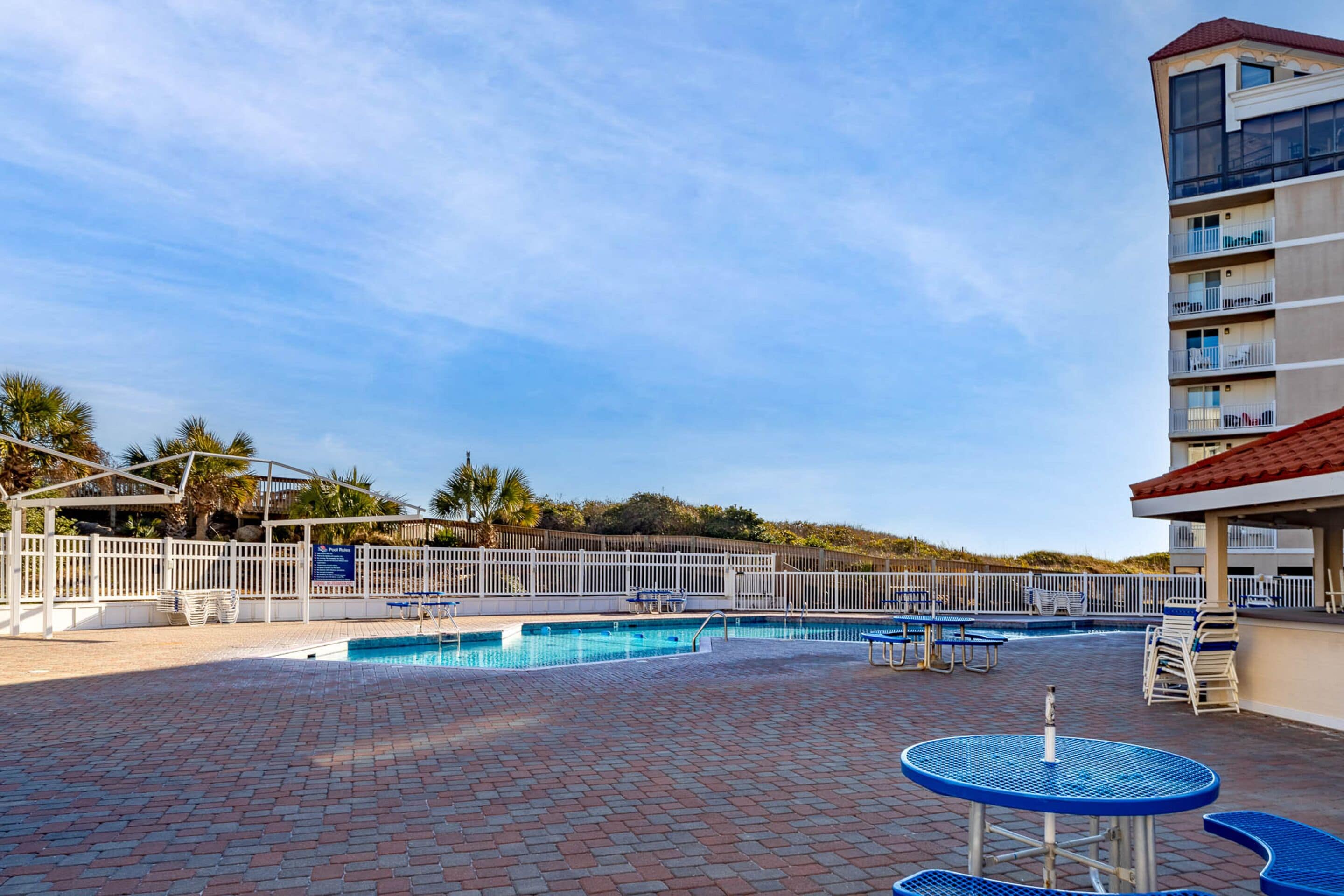 A pool area with a brick floor, blue pool tables, and a white fence.