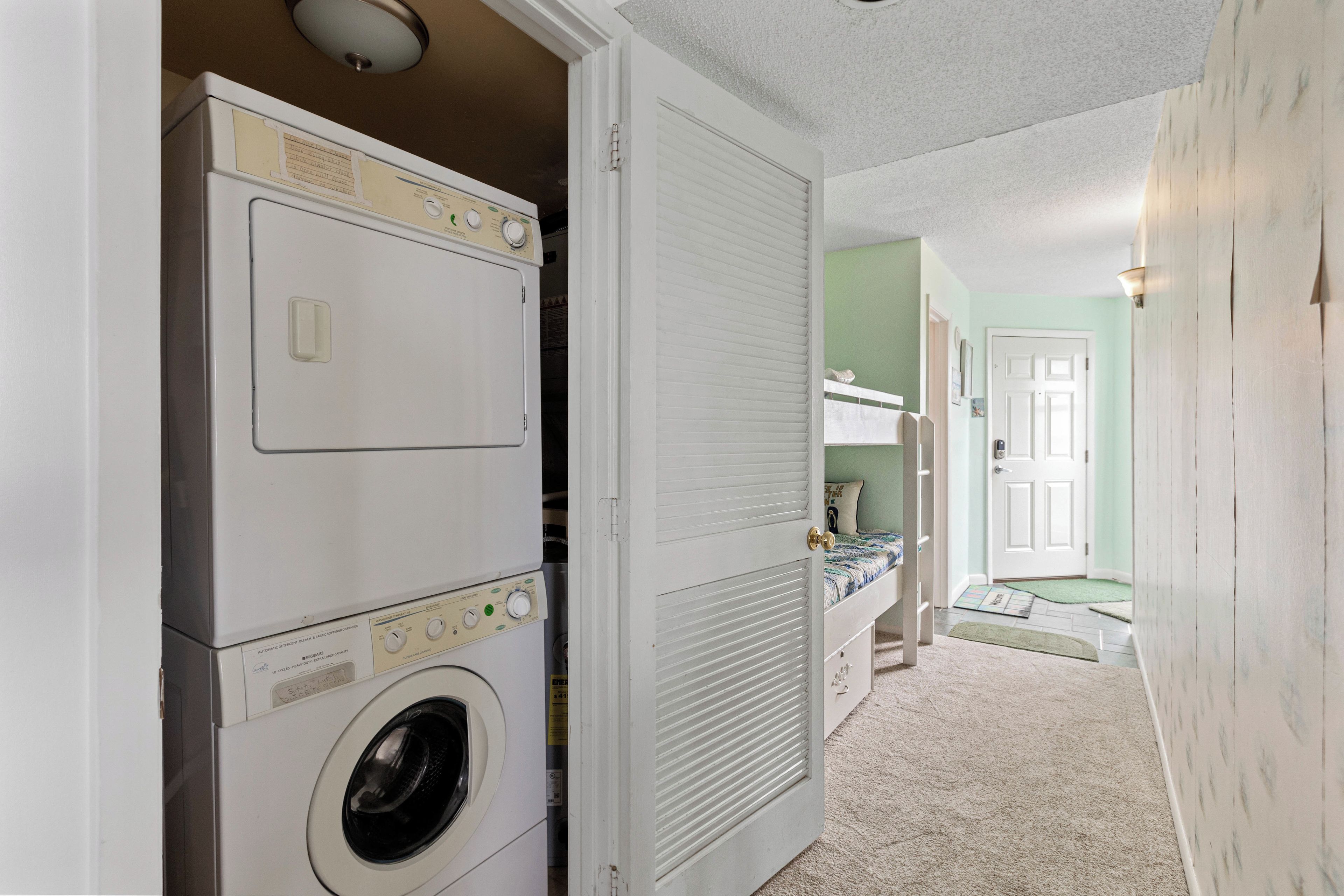A laundry room with stacked washers and dryers, a door leading to a bedroom, and a hallway with a door at the end.