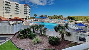A pool area with lounge chairs and umbrellas, surrounded by a white fence, with a building in the background. - St. Regis by Carolina Retreats (Sneads Ferry)