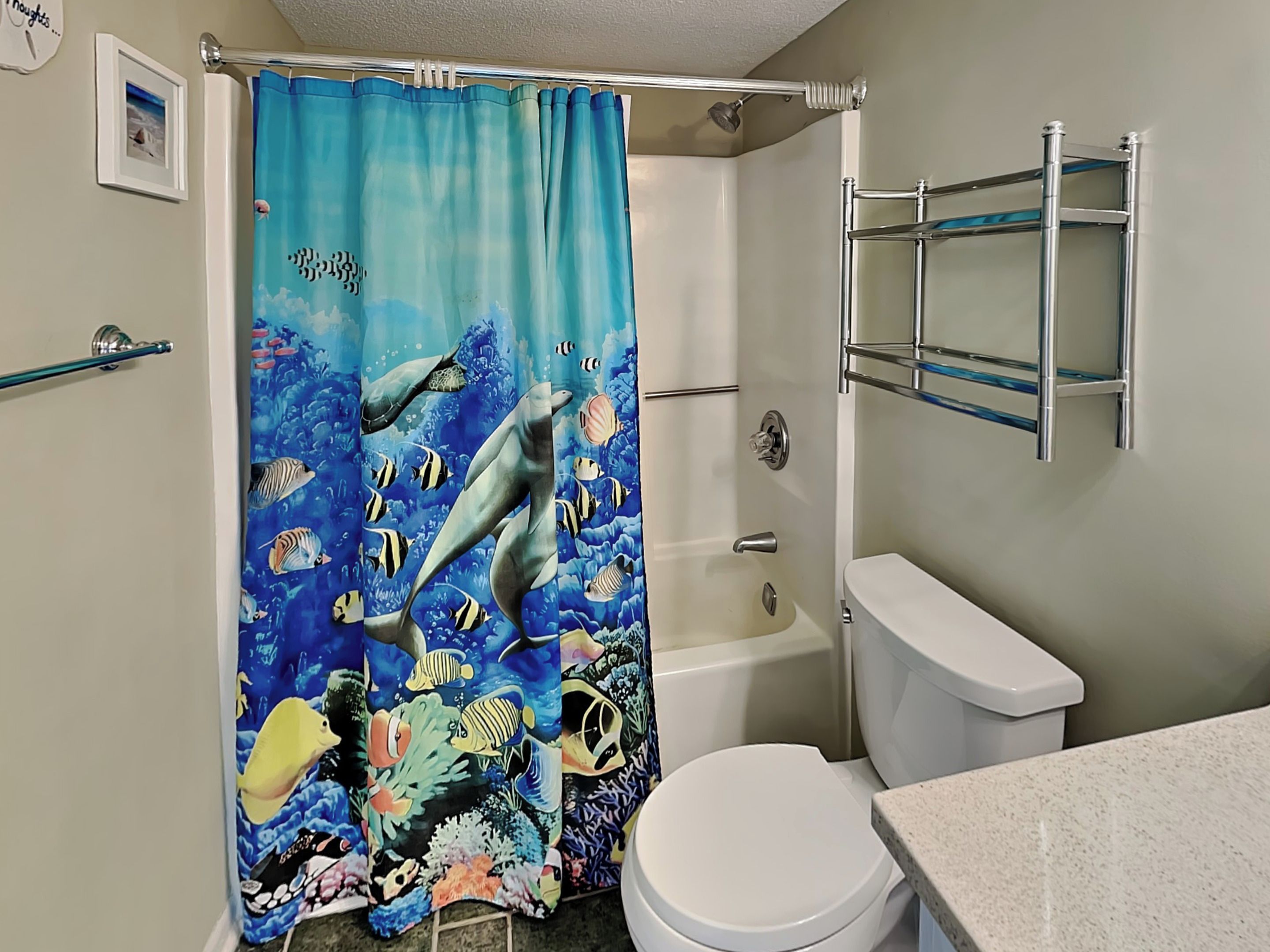 A bathroom with a shower curtain depicting underwater scenes, a bathtub, a toilet, and a metal towel rack.