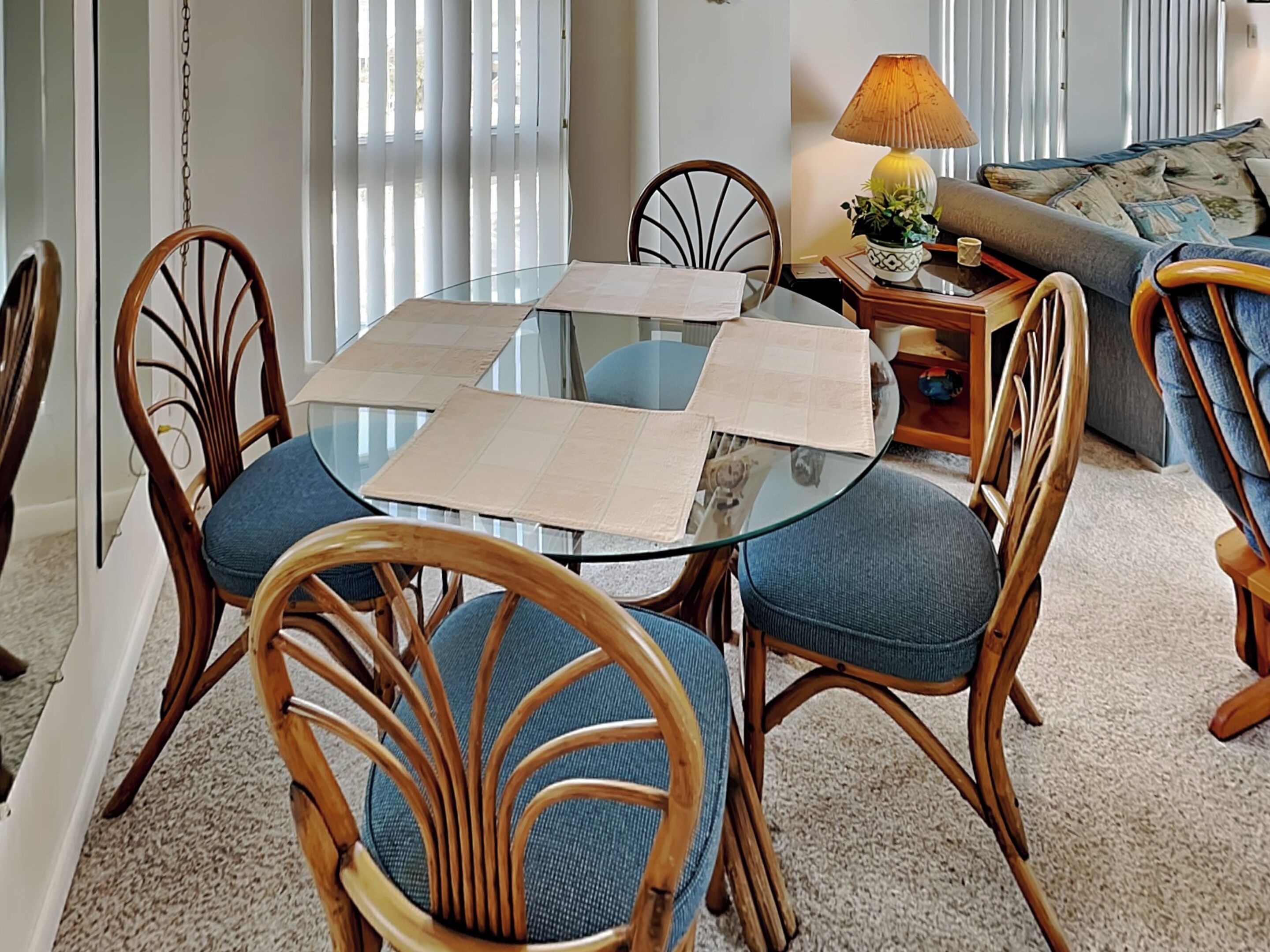 Un comedor con una mesa de vidrio rodeada de sillas de madera con cojines azules.