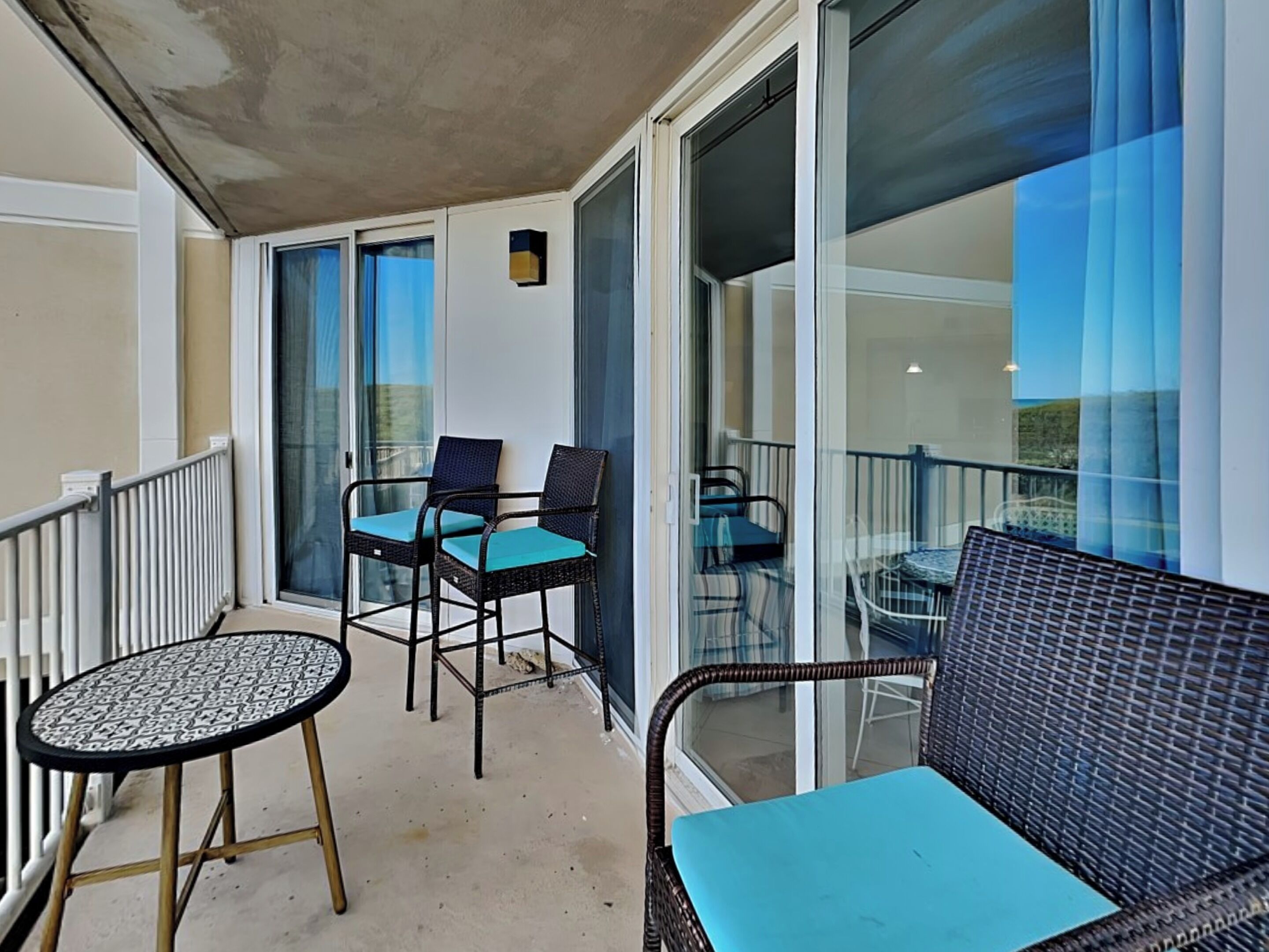 A balcony with a seating area including two chairs and a table, glass doors, and a view of the outdoors.