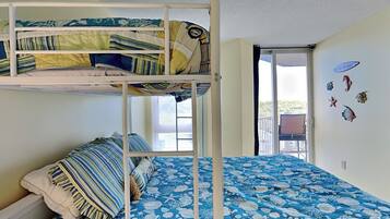 A bunk bed room with a blue patterned bedspread, a window with blinds, and a door leading to an outdoor balcony.