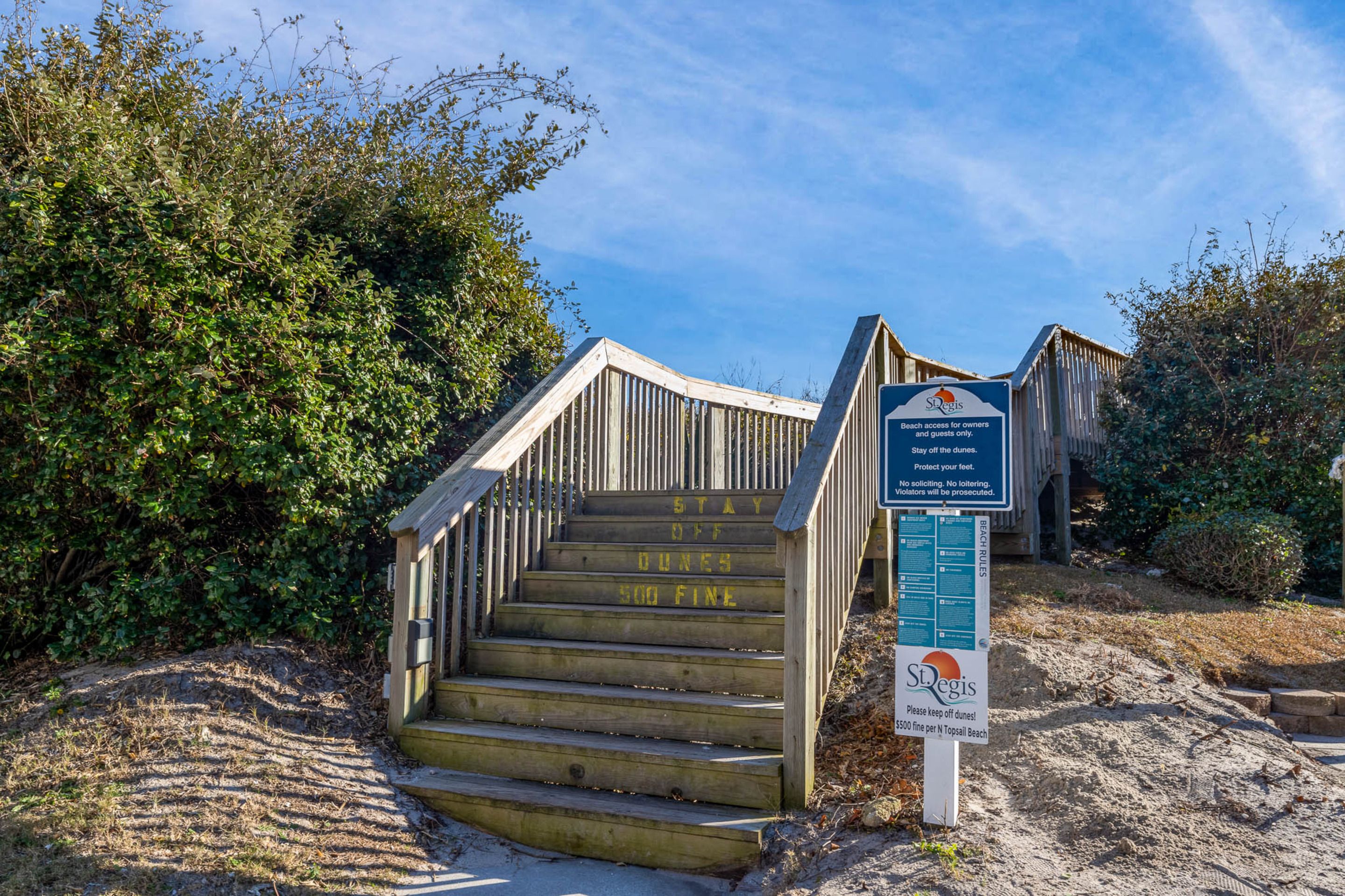 A wooden staircase leading to a beach area with a sign indicating beach access for owners and guests only, and a warning about a $500 fine for staying off the dunes.