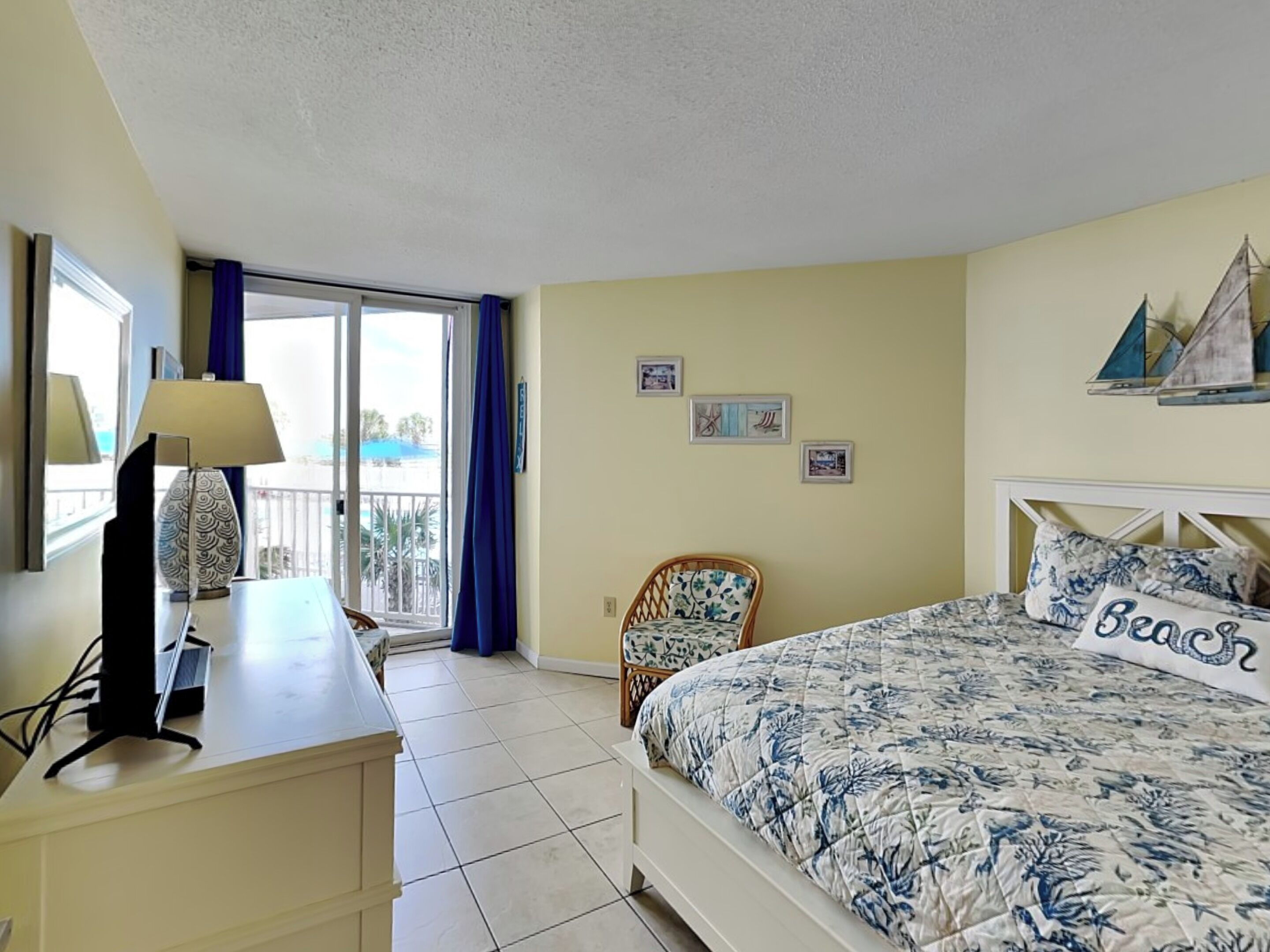 A bedroom with a bed, a desk, a chair, and a balcony with a view.