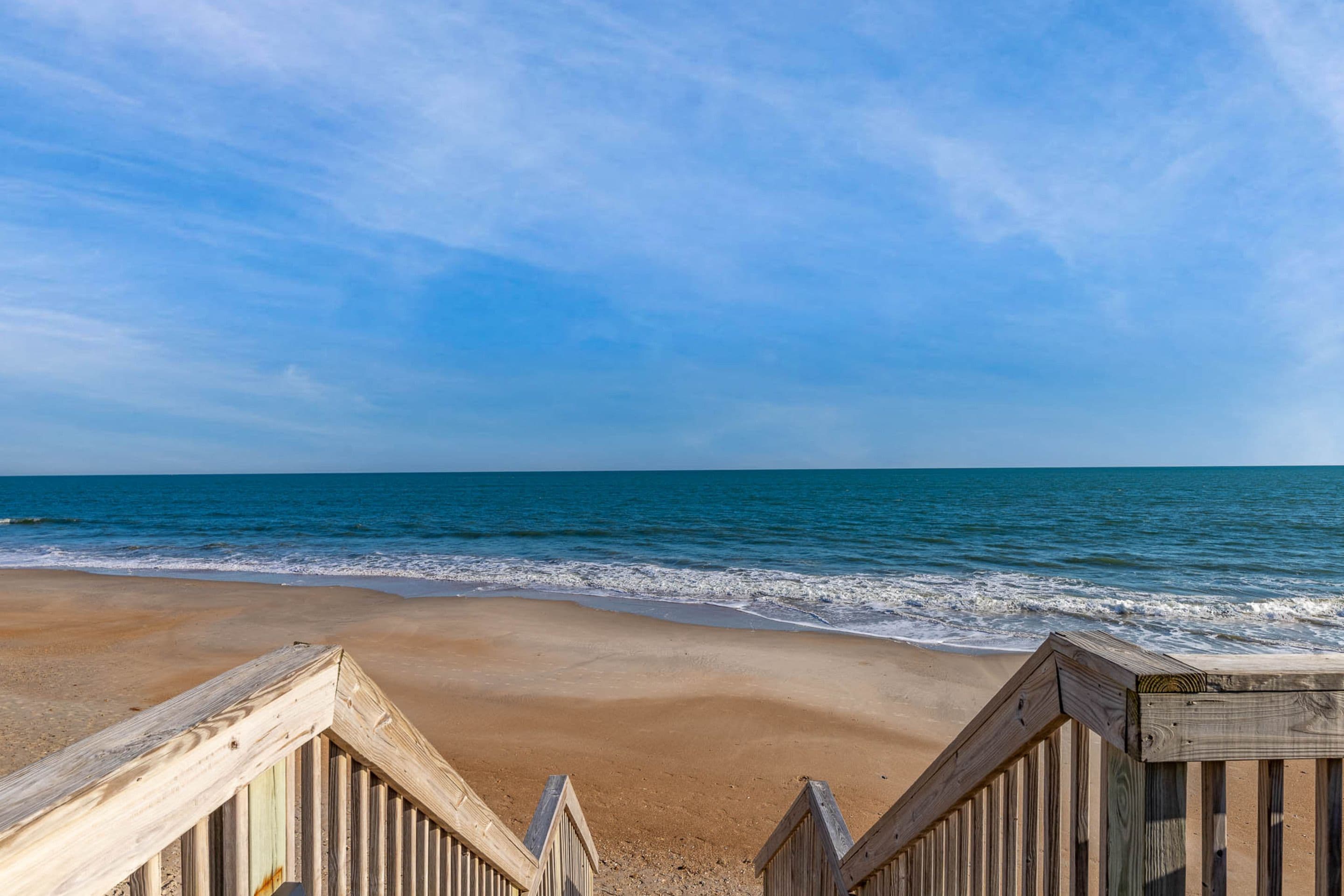 A wooden boardwalk leading to a beach with clear skies.