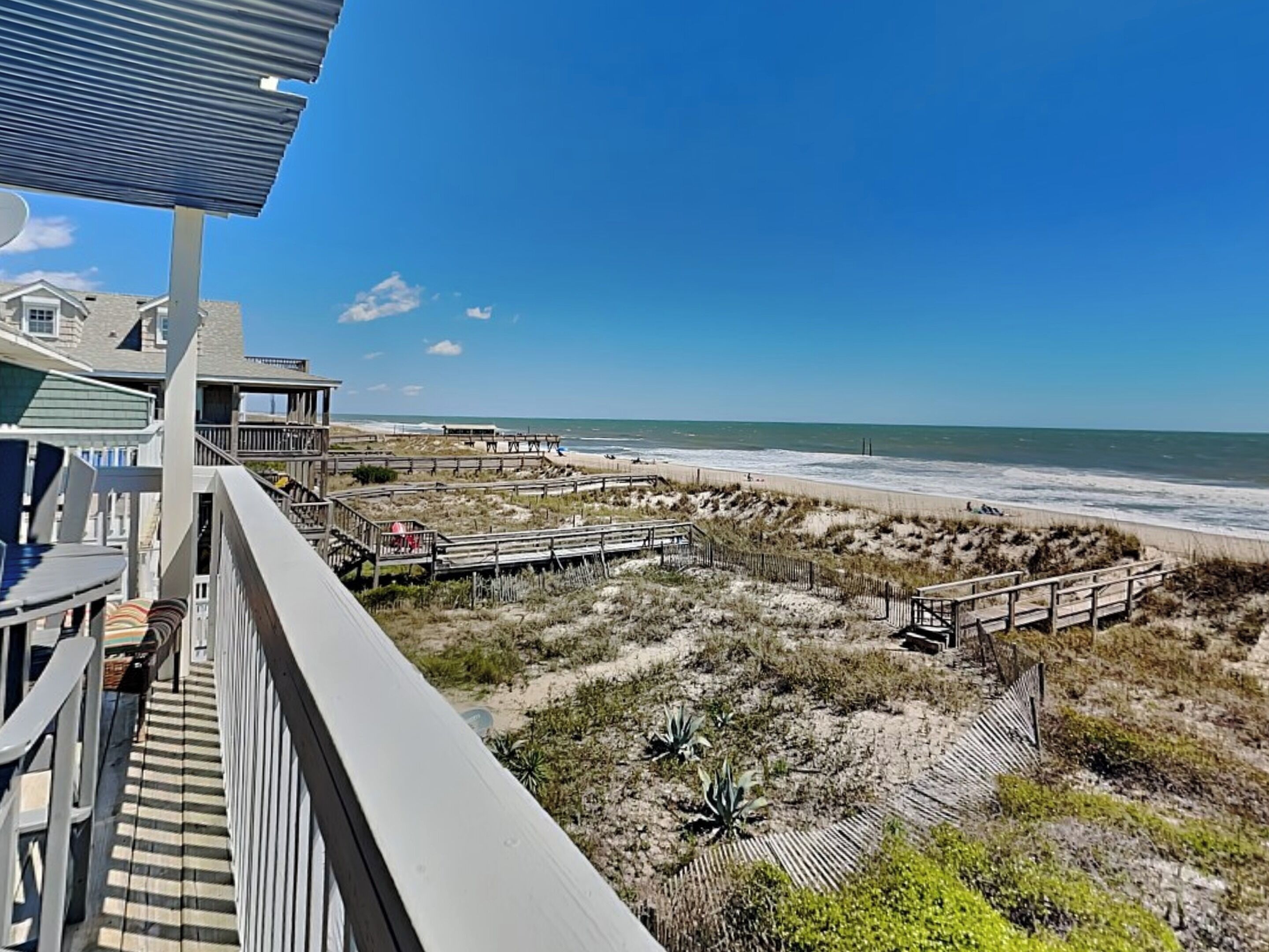 A beachfront property with a wooden deck, a beach view, and a clear sky.