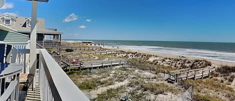 A beachfront property with a wooden deck, a beach view, and a clear sky.