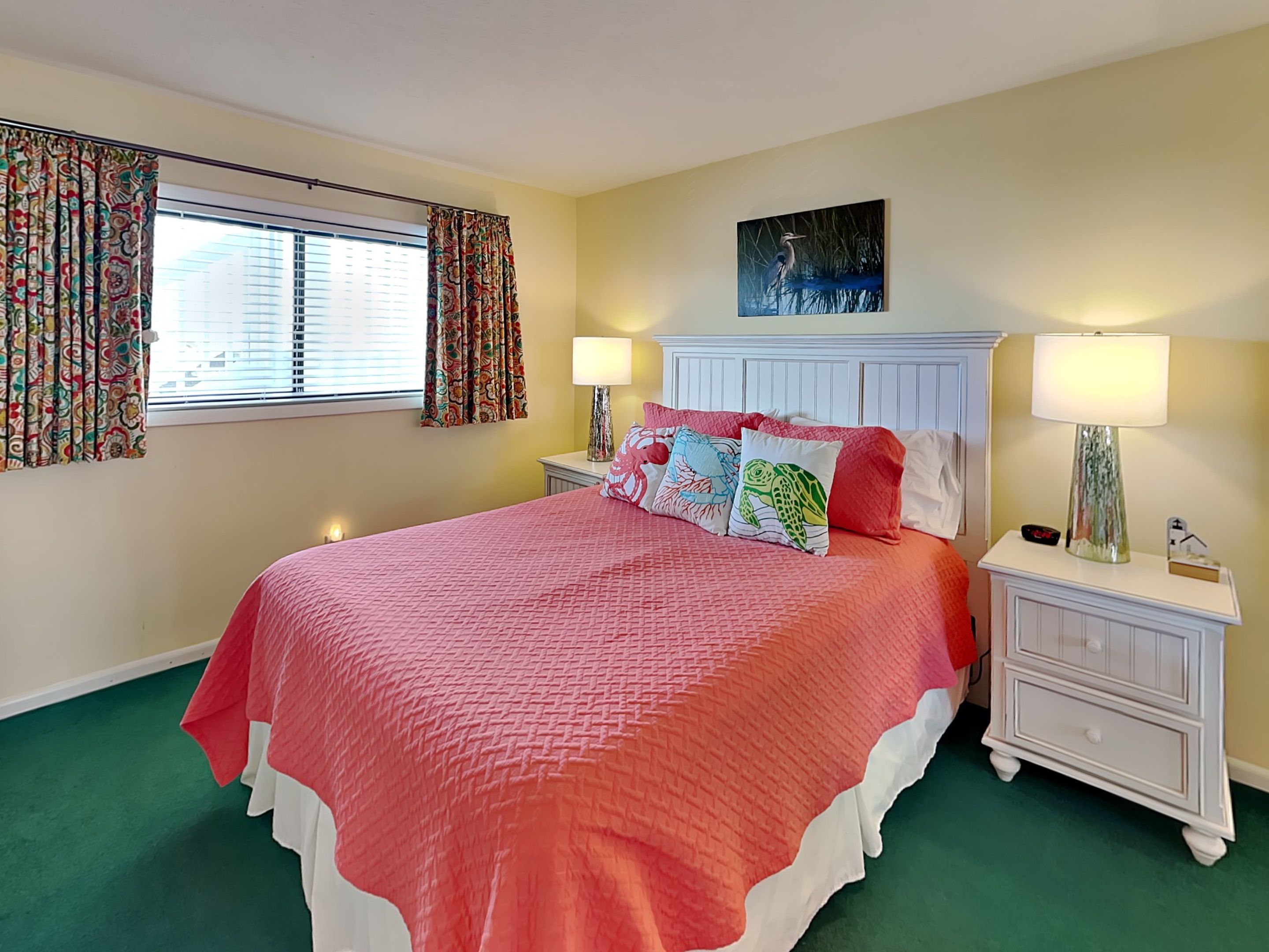 A bedroom with a large bed, two bedside tables, a nightstand, a window with curtains, and a painting on the wall.