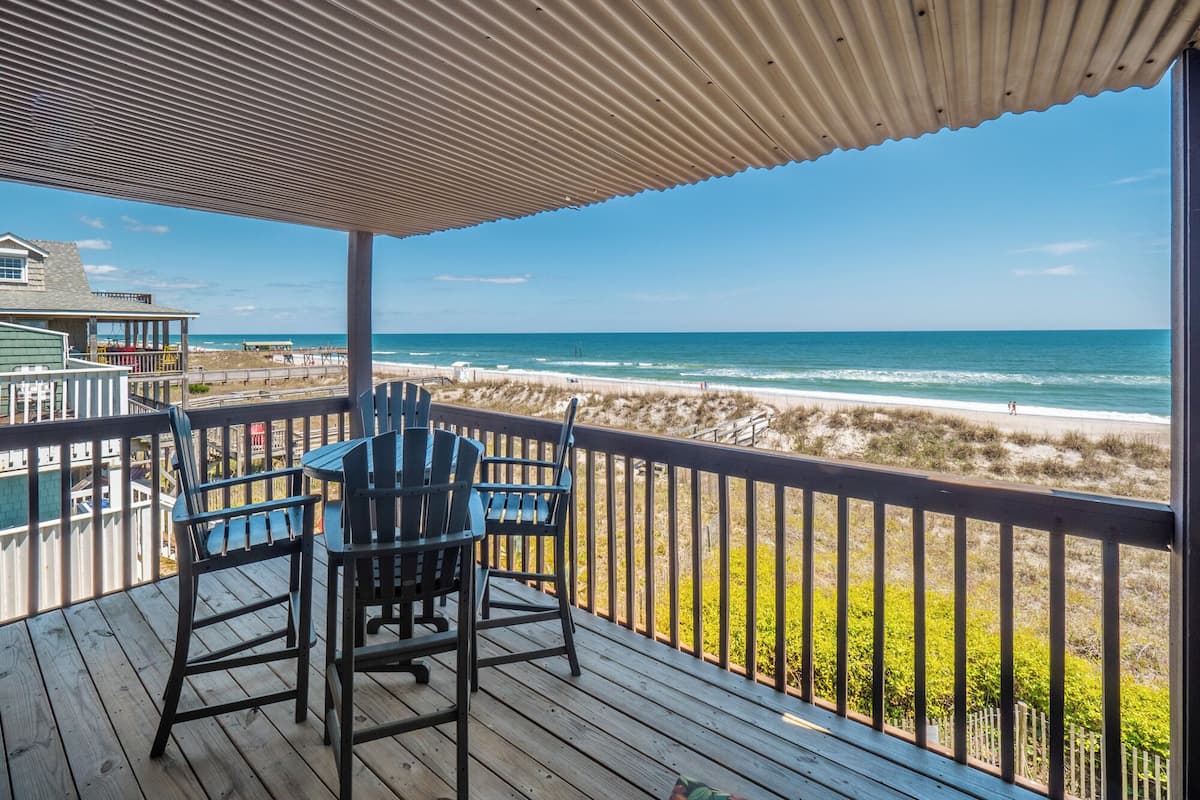 A wooden deck with Adirondack chairs overlooking a beach.