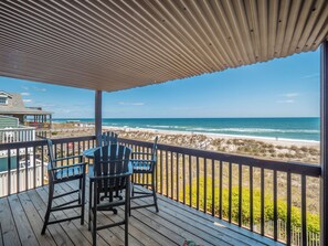 Een houten terras met Adirondack-stoelen met uitzicht op een strand.