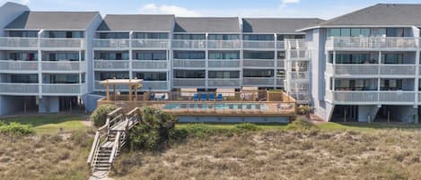 Un hotel de varios pisos con balcones, un área de piscina y una playa arenosa frente a él.