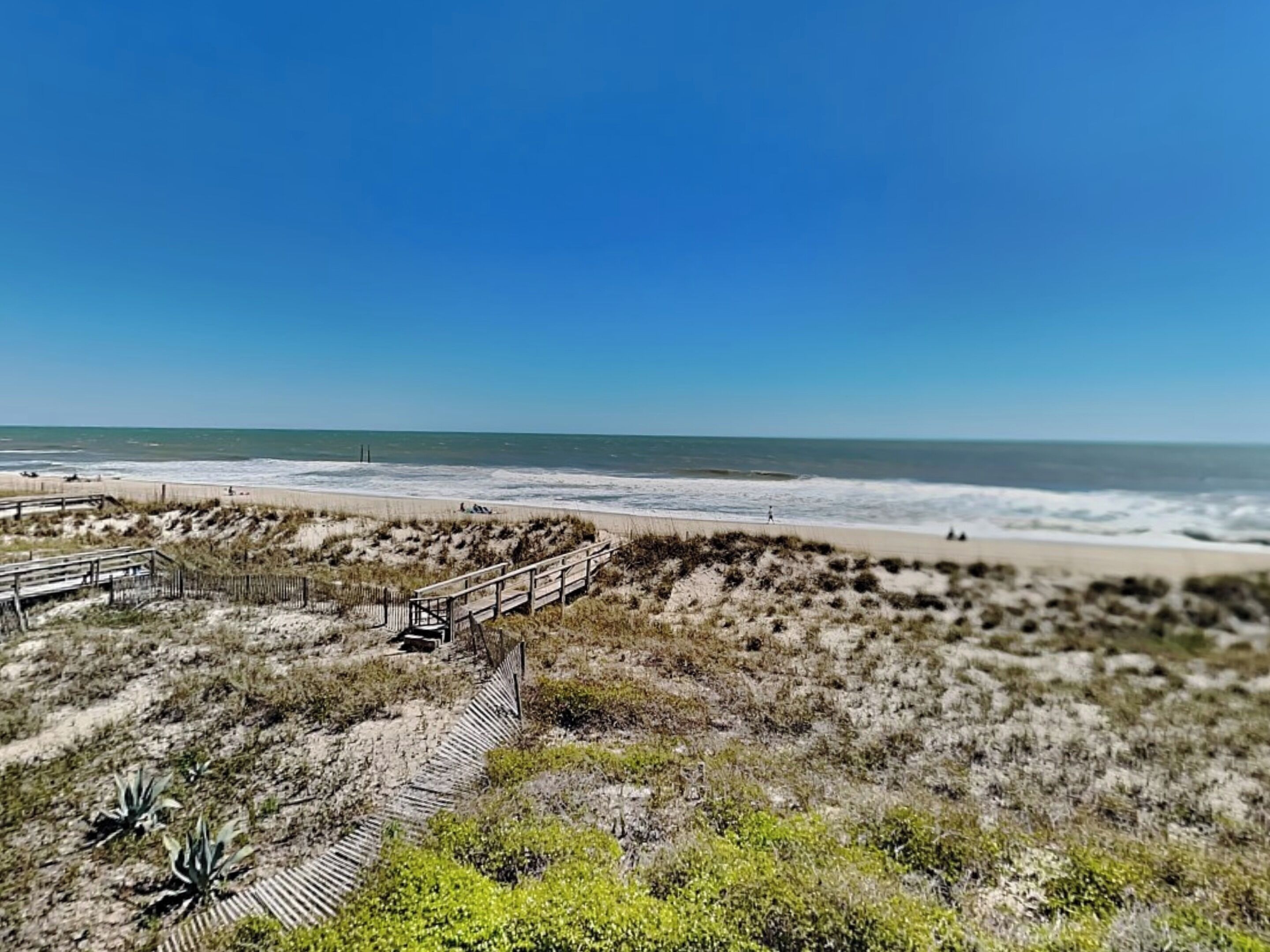 Une plage avec une promenade en bois qui mène au rivage, des dunes de sable et l’océan.