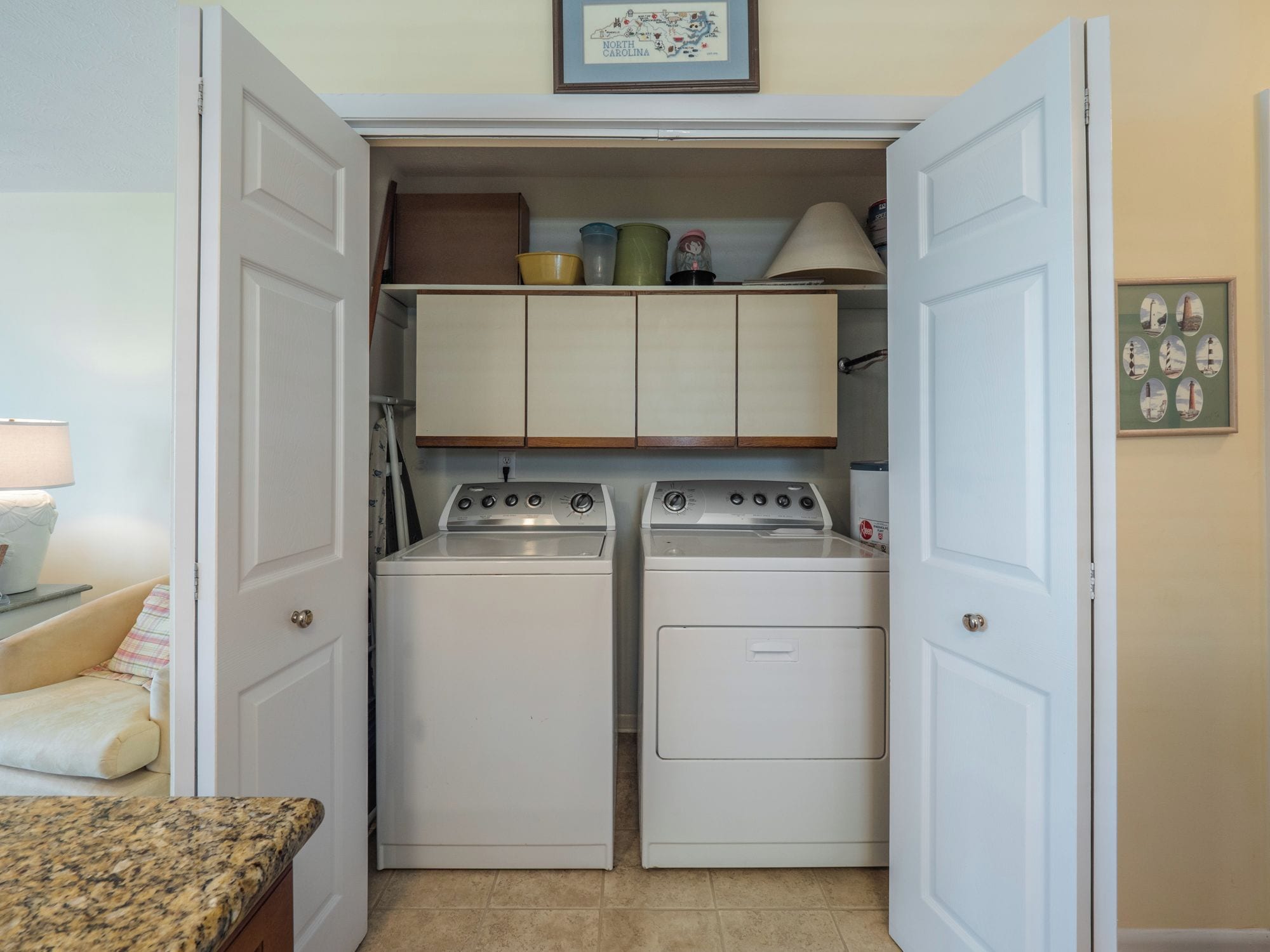 A laundry room with two washing machines and a dryer, a small cabinet above the machines, and a framed map on the wall.