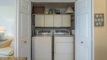 A laundry room with two washing machines and a dryer, a small cabinet above the machines, and a framed map on the wall.