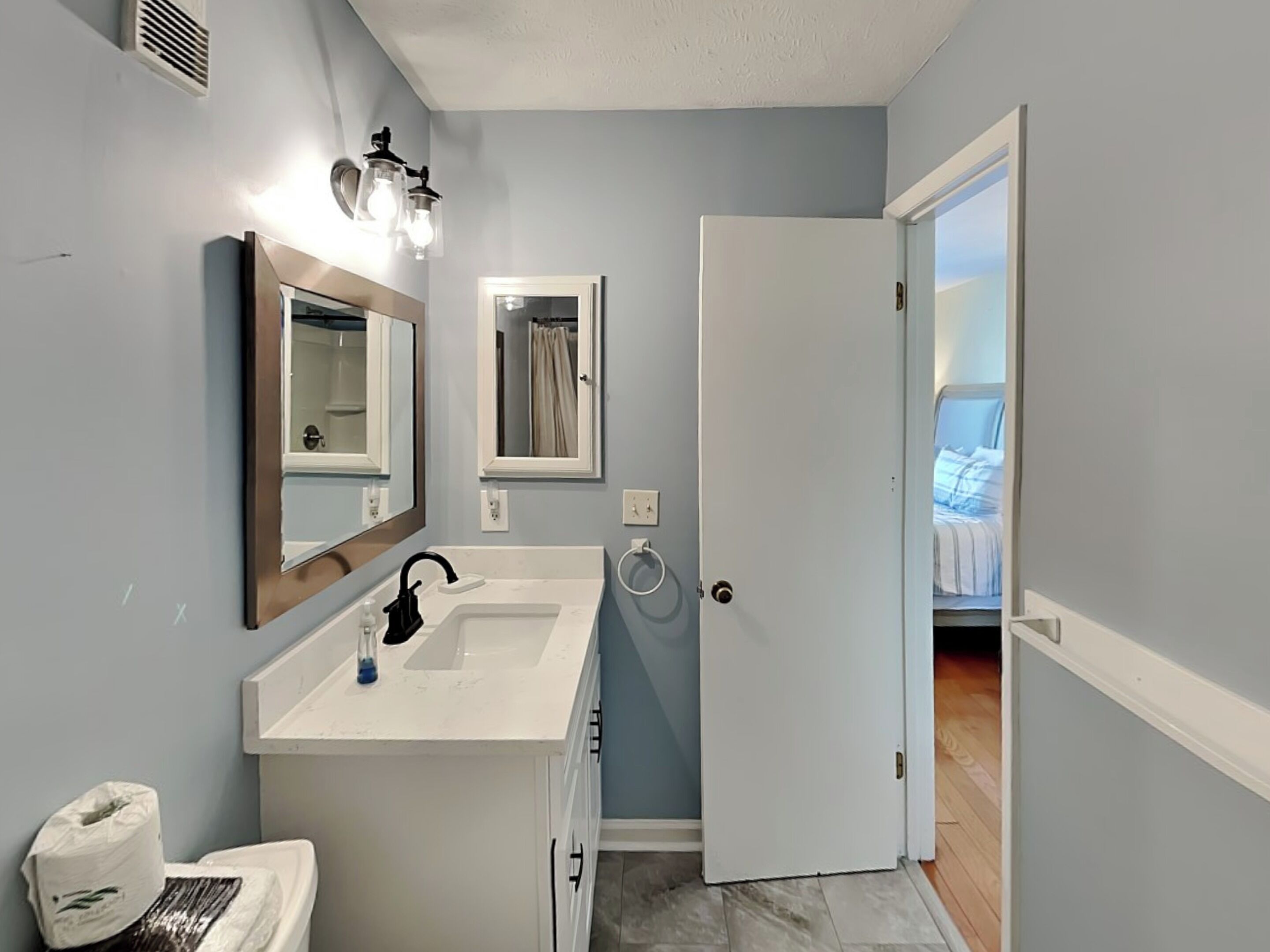A bathroom with a white sink, two mirrors, a towel rack, and a toilet.