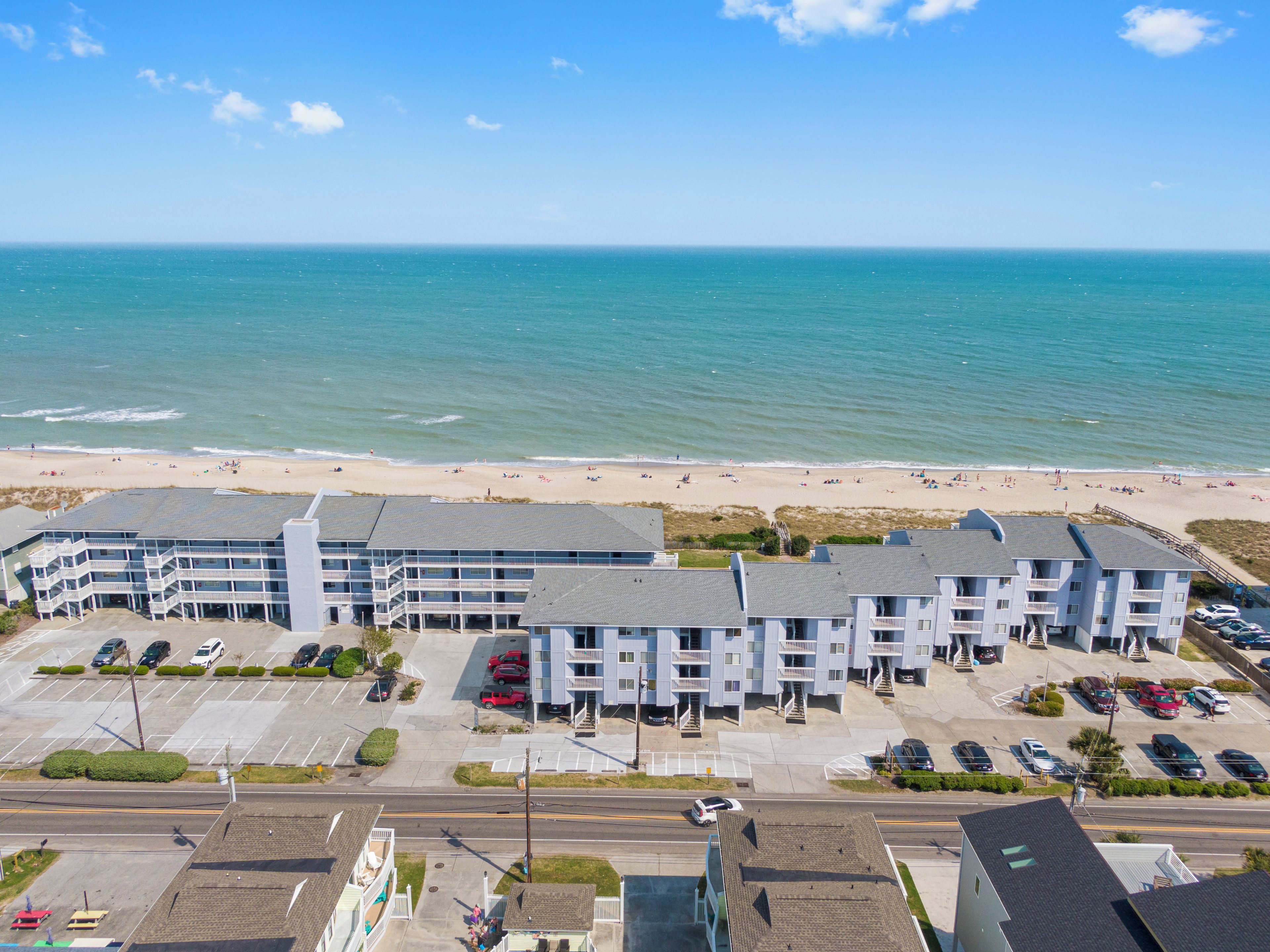 A coastal hotel with multiple floors, a parking lot, and a beach view.
