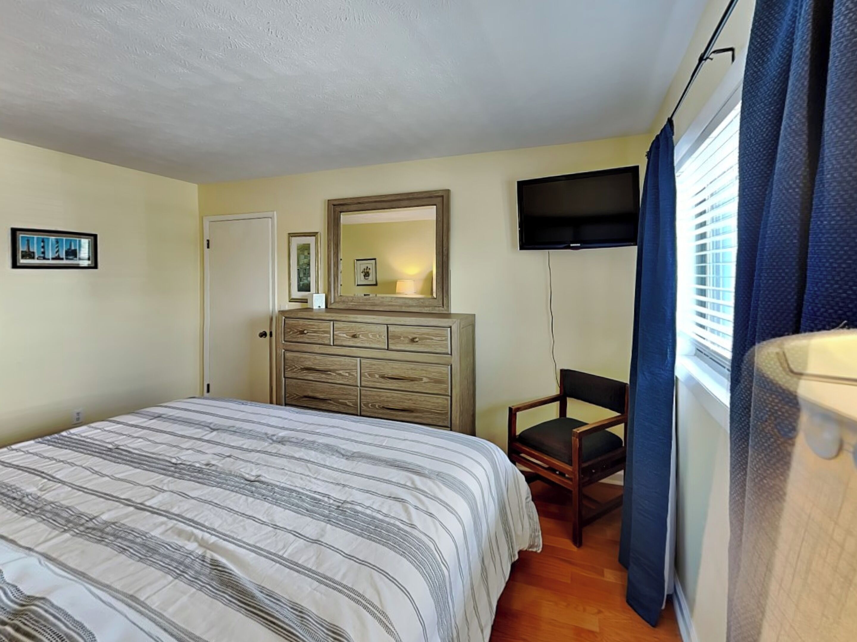 A bedroom with a bed, a dresser, a chair, a TV, and a window with curtains.