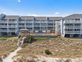 Un hotel de varios pisos con balcones, un área de piscina y una playa arenosa frente a él.