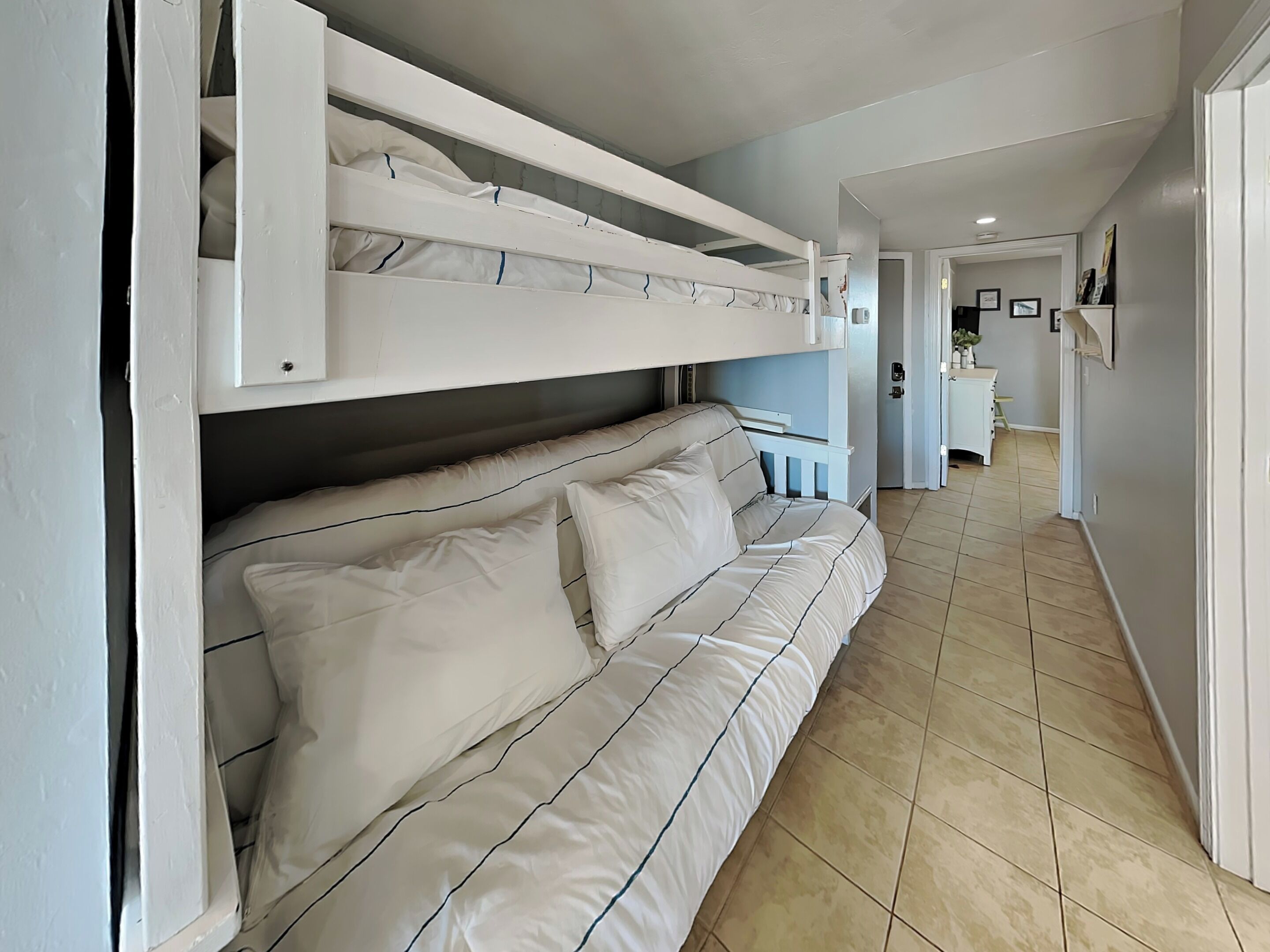 A room with a bunk bed, a sofa, and a kitchen area in the background.