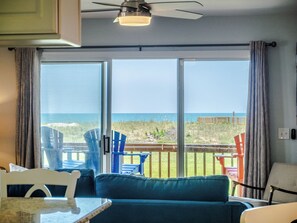 A room with a view of the ocean, a ceiling fan, and a table with chairs.