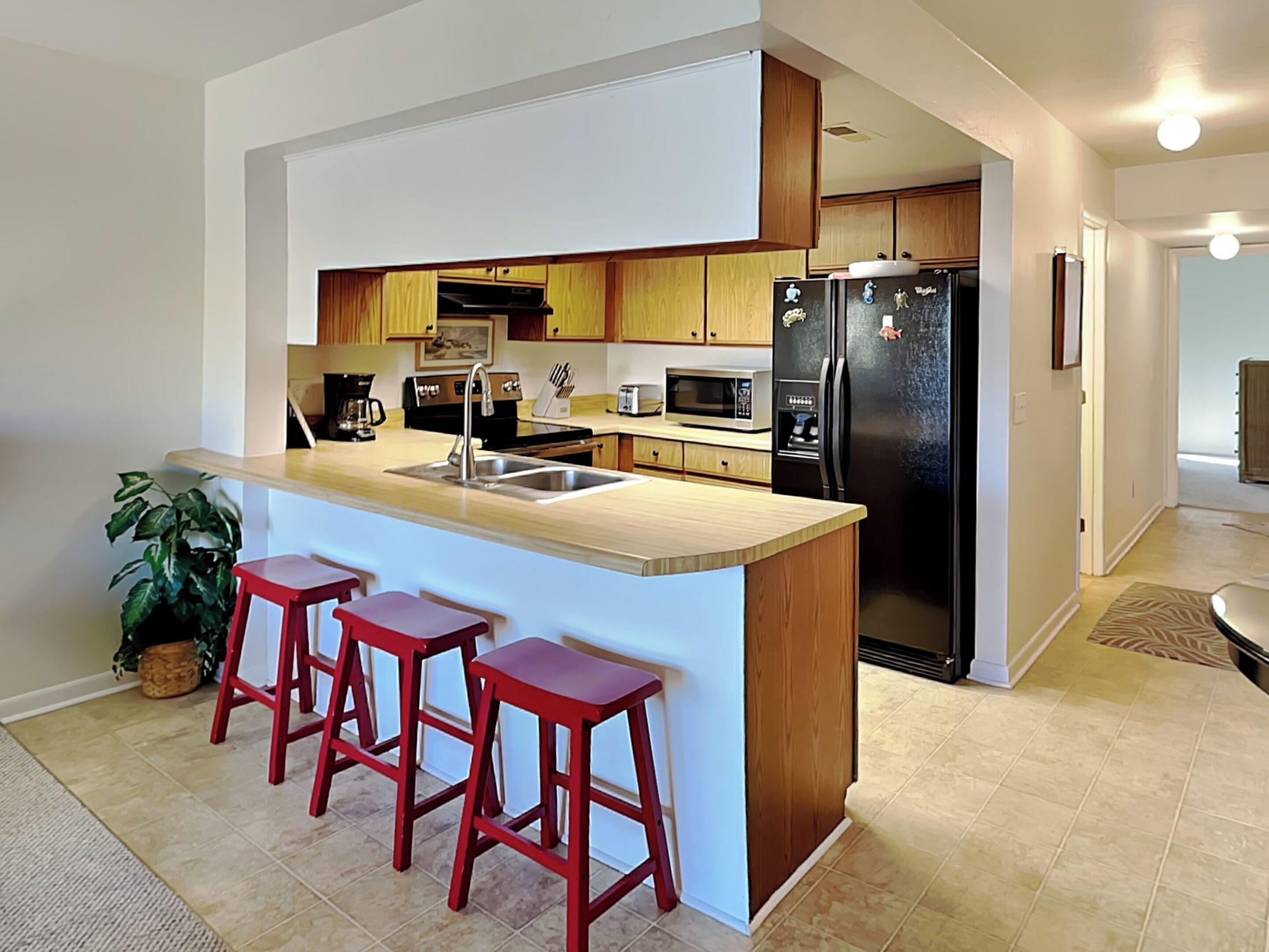 A modern kitchen with a central island, wooden cabinets, stainless steel appliances, and three red bar stools.