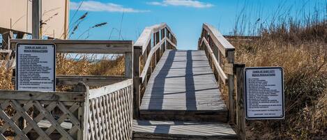 A wooden boardwalk leading to a beach with signs listing beach regulations.