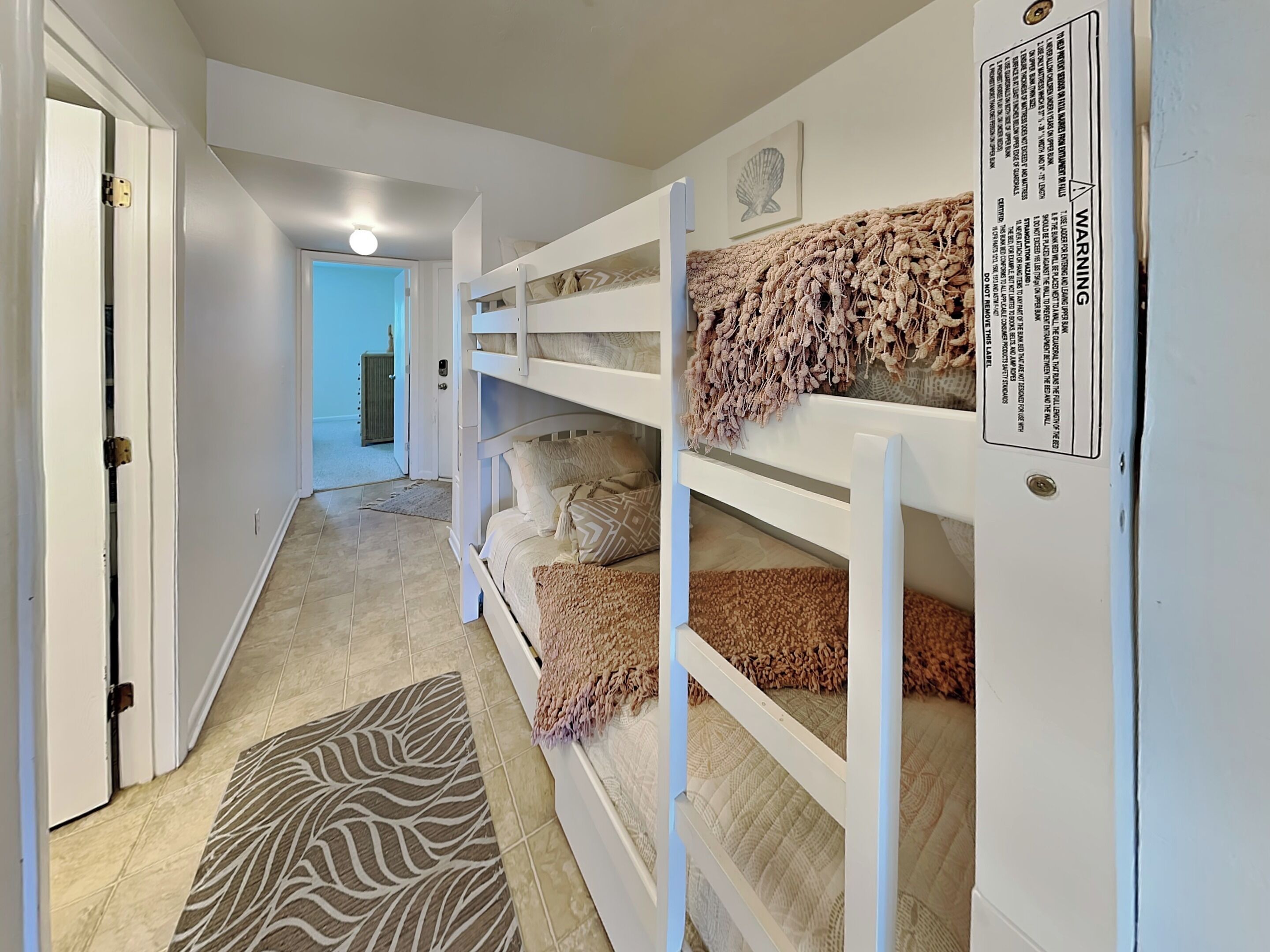 A bunk bed with a warning label, a zebra-patterned rug, and a door leading to another room.