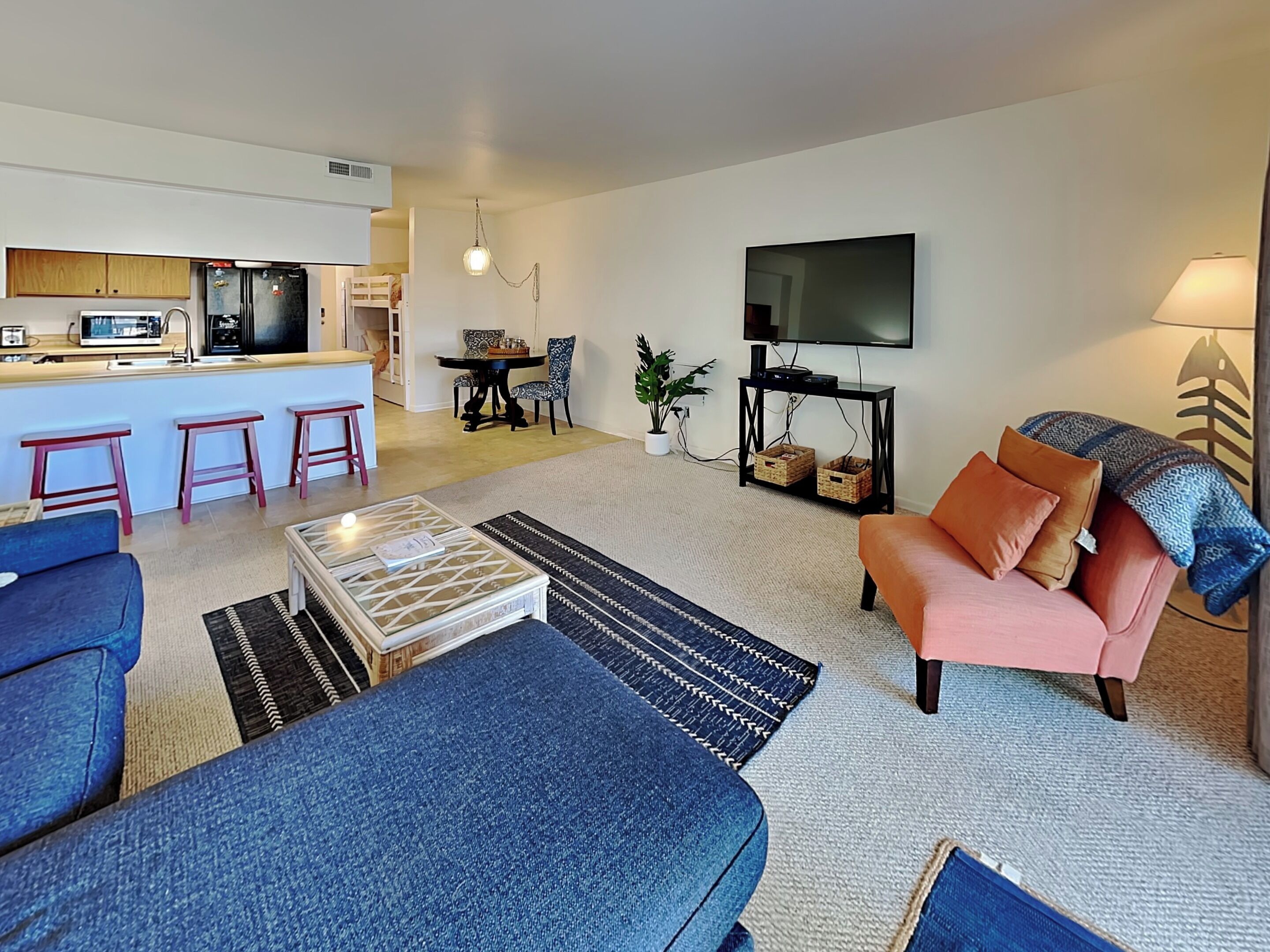 Ein modernes Wohnzimmer mit einer Couch, einem Couchtisch und einem Fernseher. Im Hintergrund ist eine Küchenzeile zu sehen.