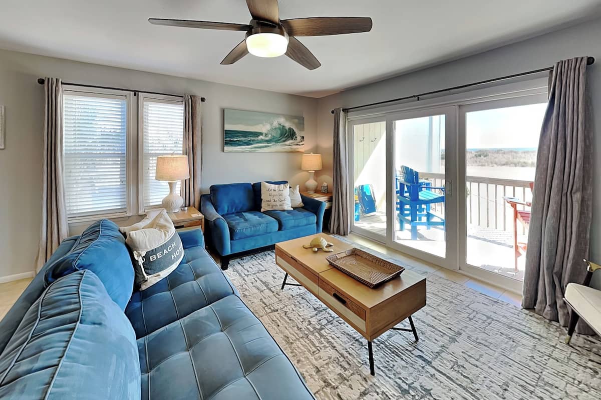 A spacious living room with a large blue sofa, a wooden coffee table, and a ceiling fan.