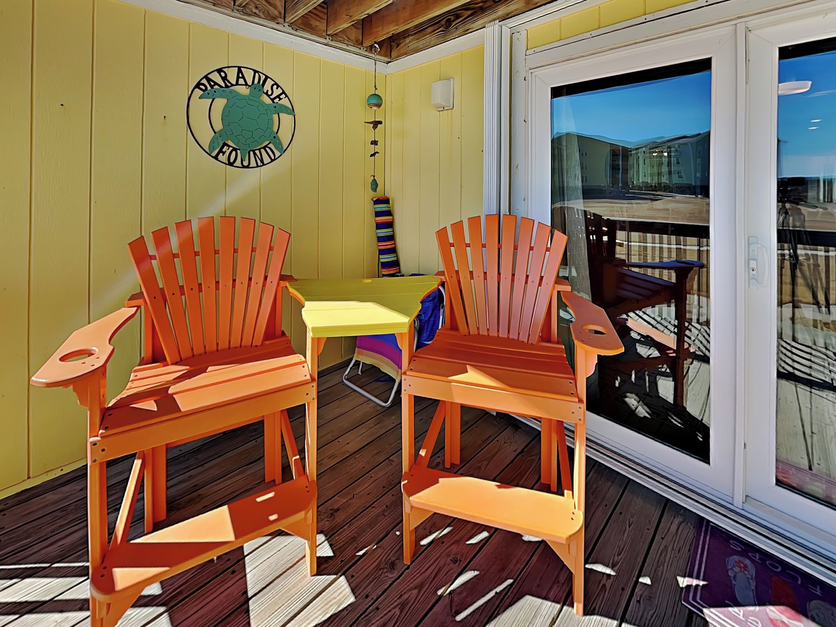 A wooden deck with two Adirondack chairs, a small table, and a sign reading "Paradise Found".