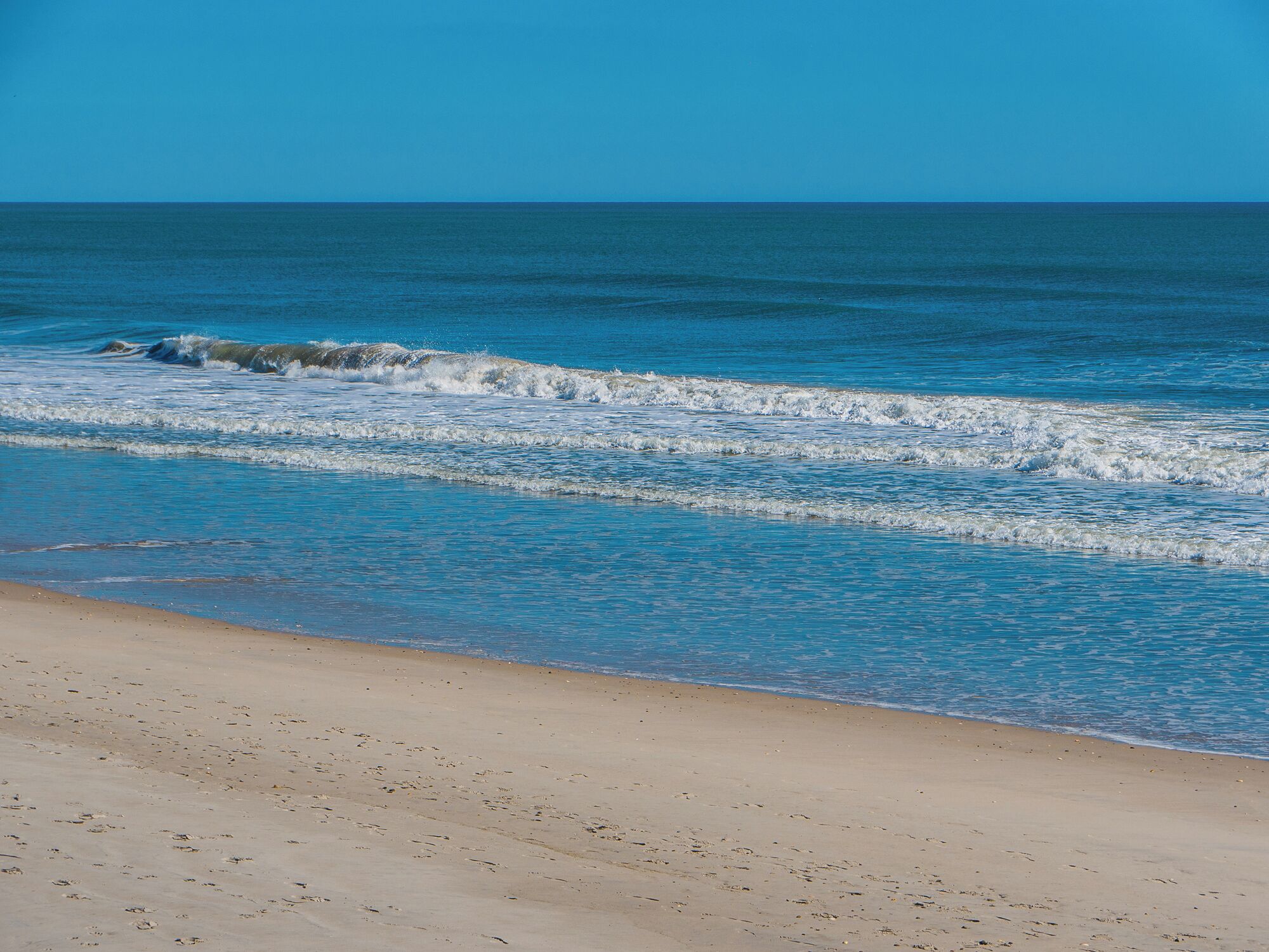 A beach with clear blue water and a sandy shore.