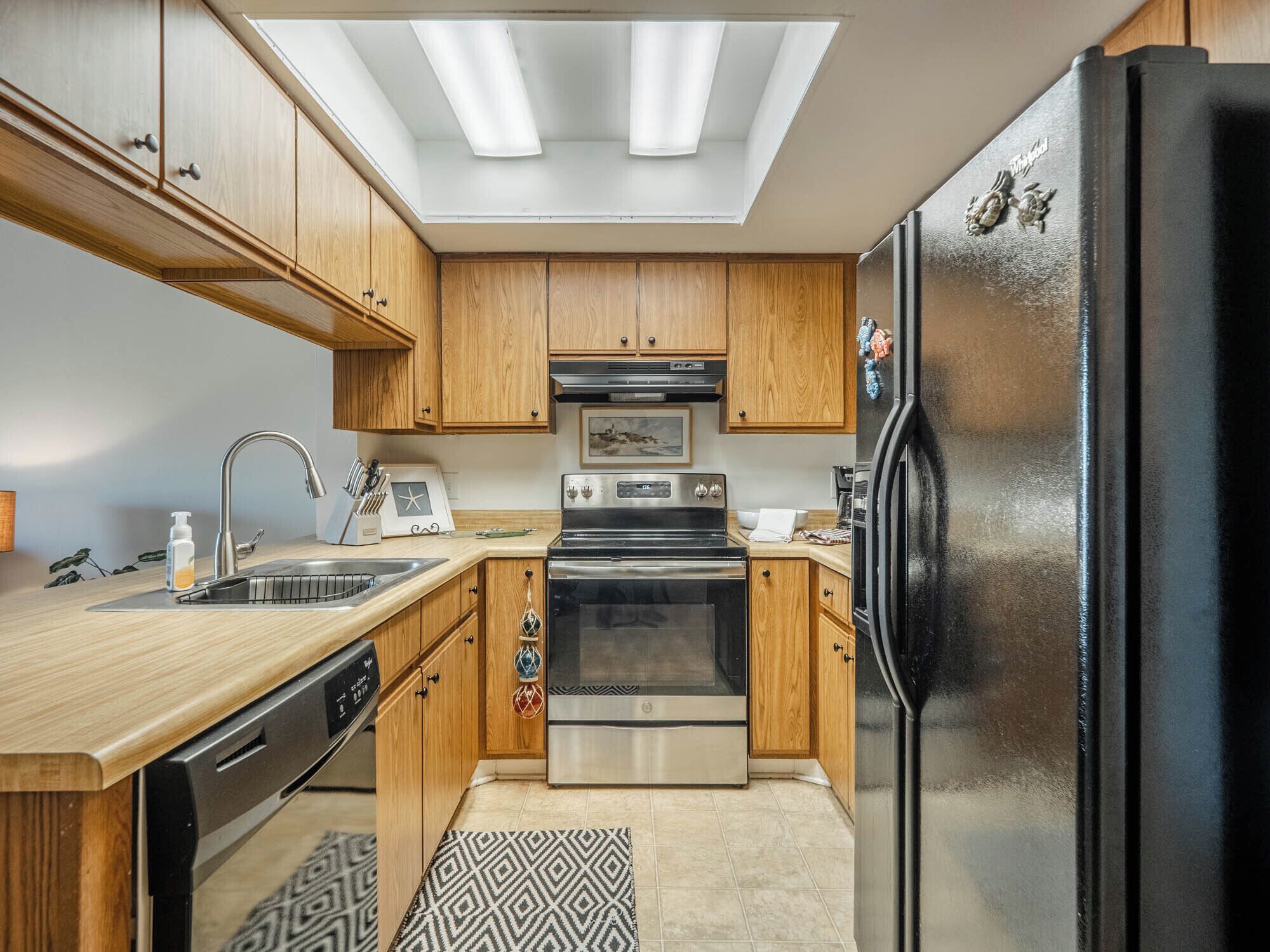 Una cocina moderna con armarios de madera, un refrigerador negro, electrodomésticos de acero inoxidable y un tragaluz.