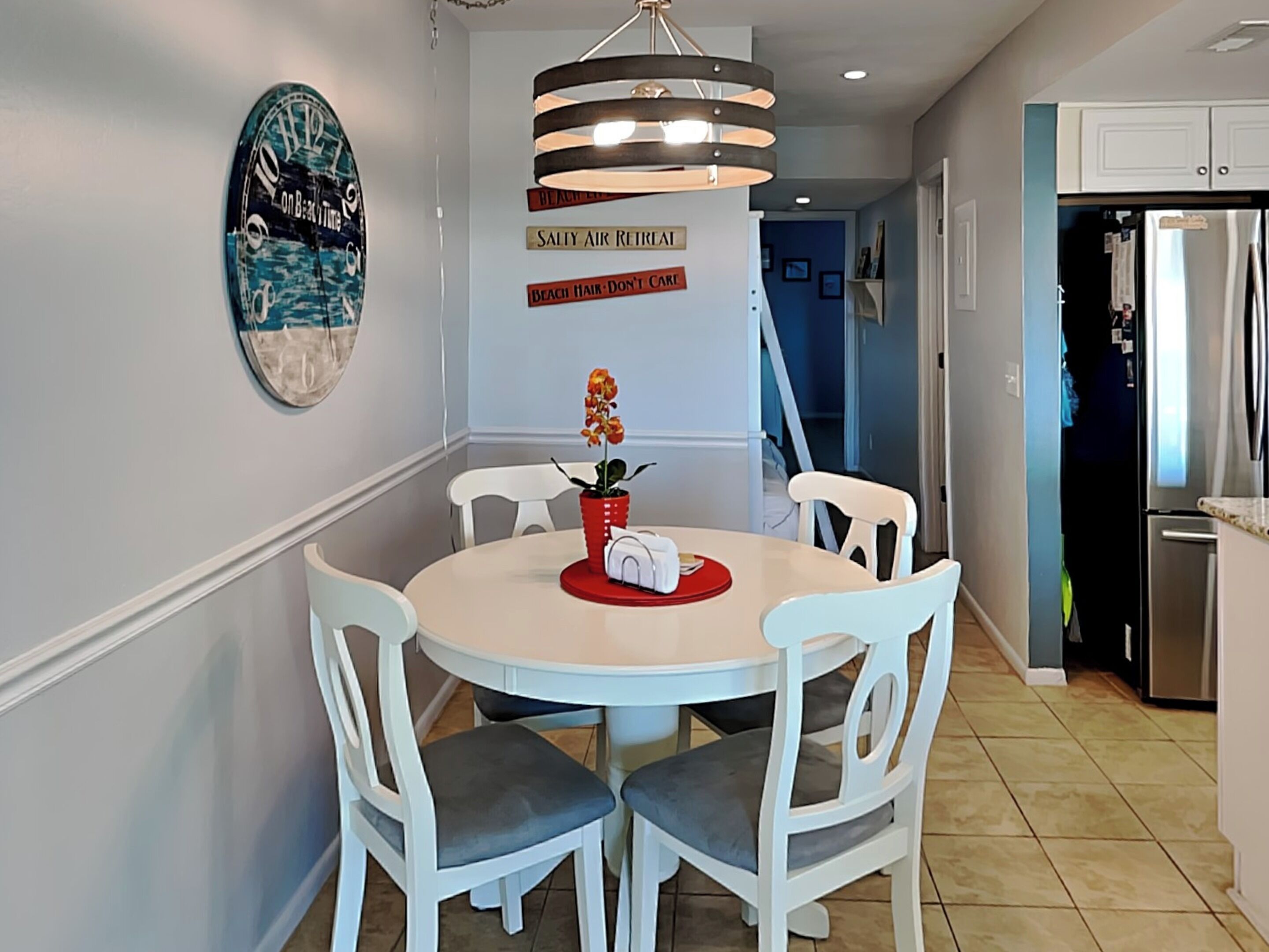 A dining area with a round table, white chairs, a red placemat, and a potted plant.