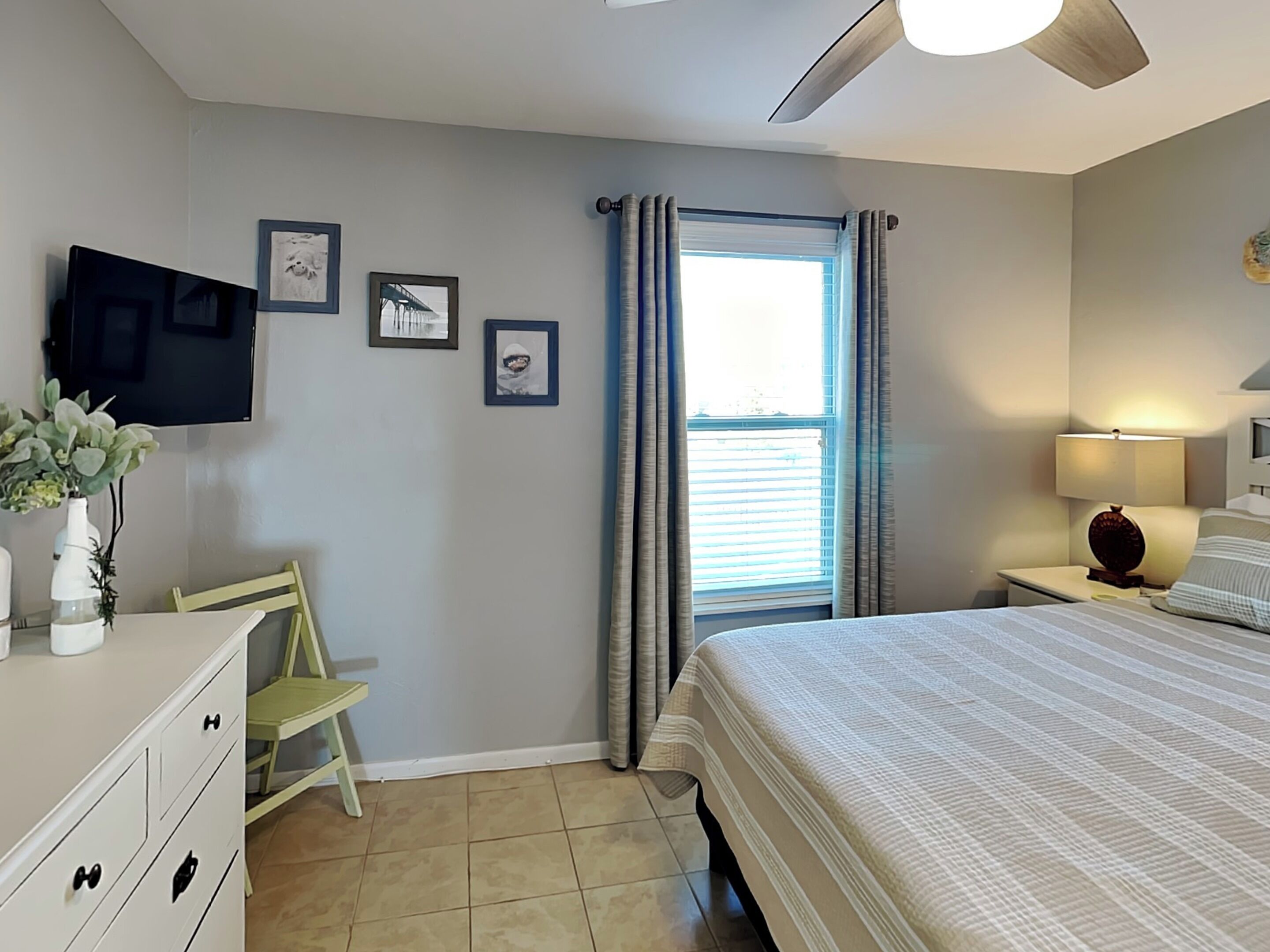 Une chambre à coucher avec un lit, un bureau, une chaise, un téléviseur et une fenêtre avec des rideaux.