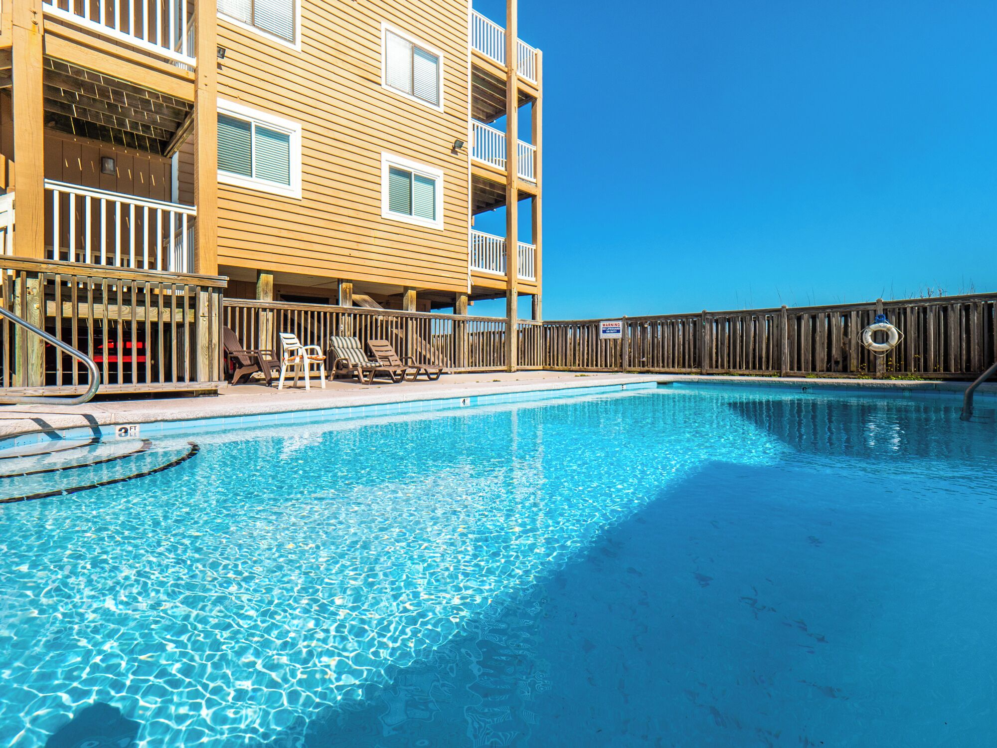 A swimming pool with lounge chairs and a wooden fence.