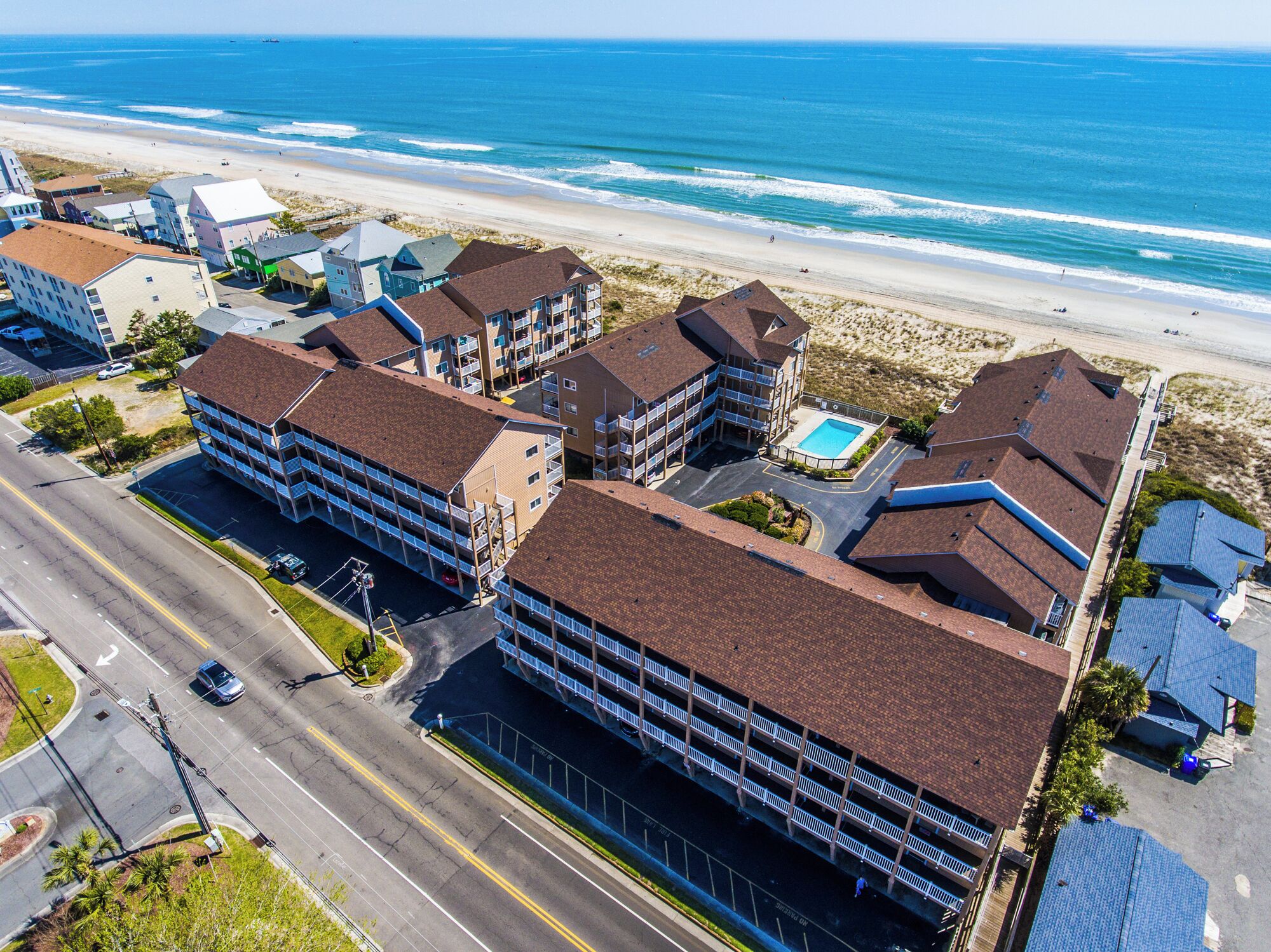 Un hotel costero con varias edificaciones, un estacionamiento y vista a la playa.