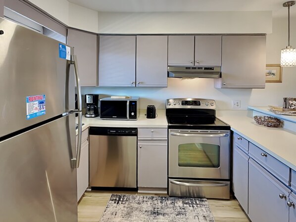 A modern kitchen with stainless steel appliances, including a refrigerator, microwave, dishwasher, and oven. - Sand Pebbles by Carolina Retreats (Carolina Beach)