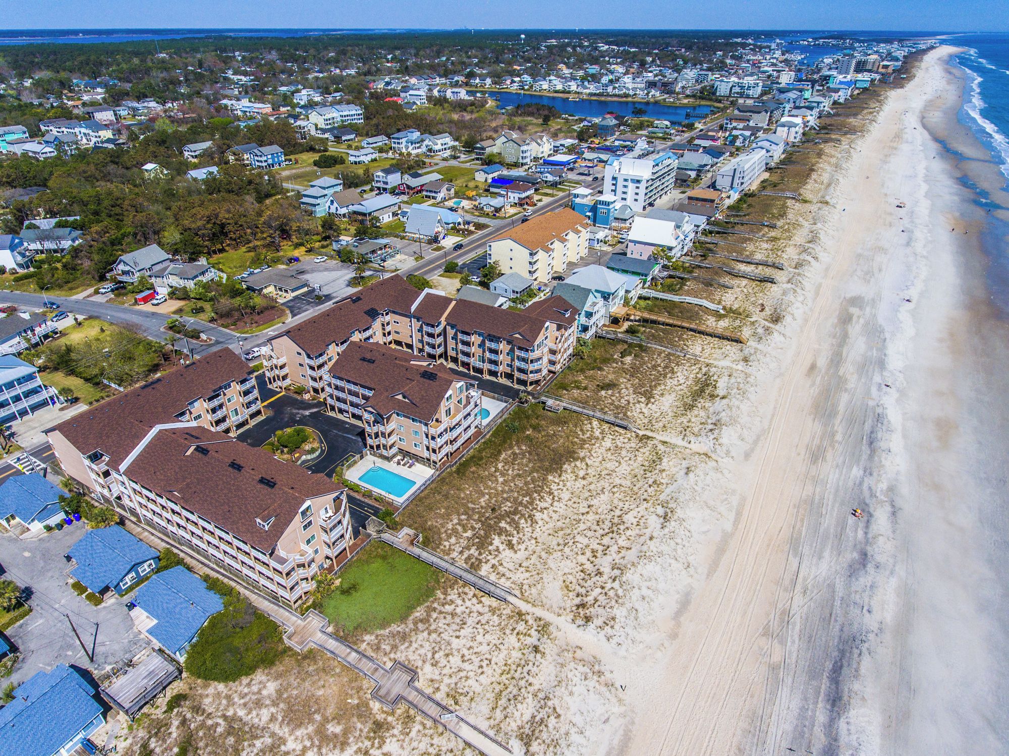 An aerial view of a coastal residential area with beachfront properties, including multi-story buildings with balconies and a beach access walkway.