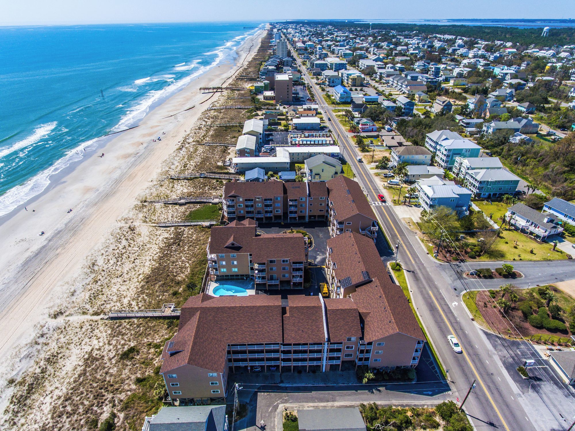 An aerial view of a coastal hotel with multiple buildings, a beach, and a road.