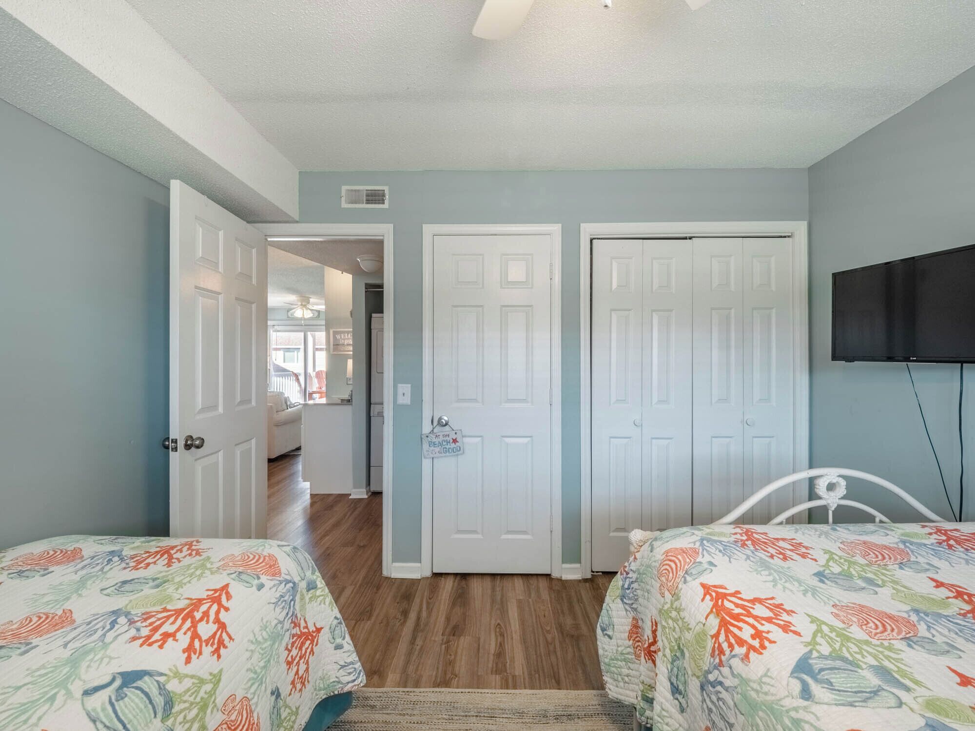 A bedroom with two beds, a television, and a hallway leading to another room.
